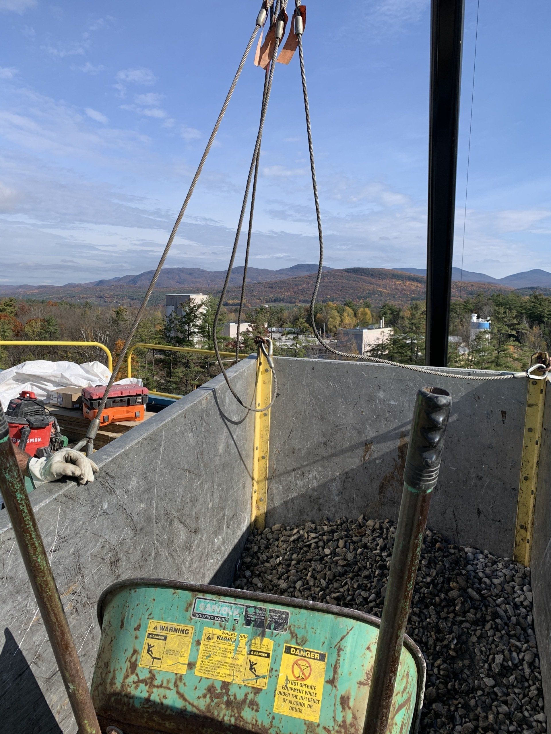 A green wheelbarrow is being lifted by a crane.