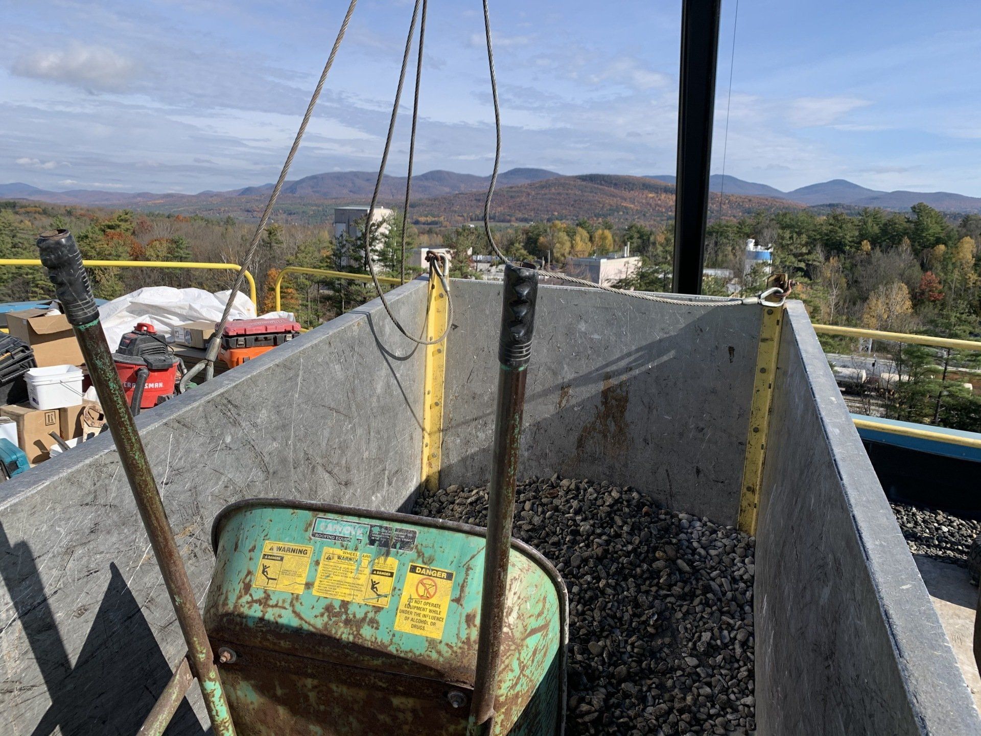 A green wheelbarrow is being lifted by a crane.