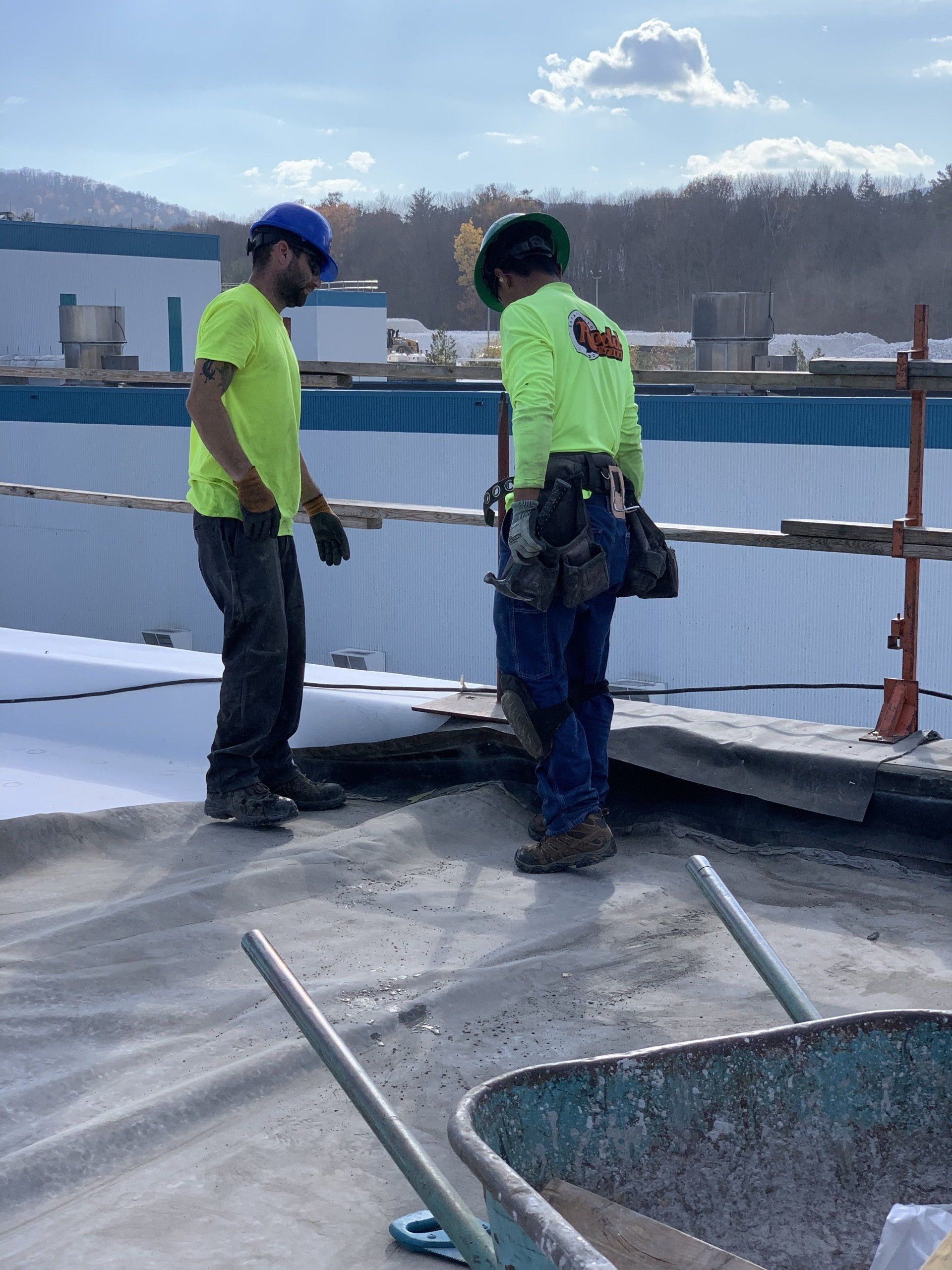 Two construction workers are standing on top of a roof.