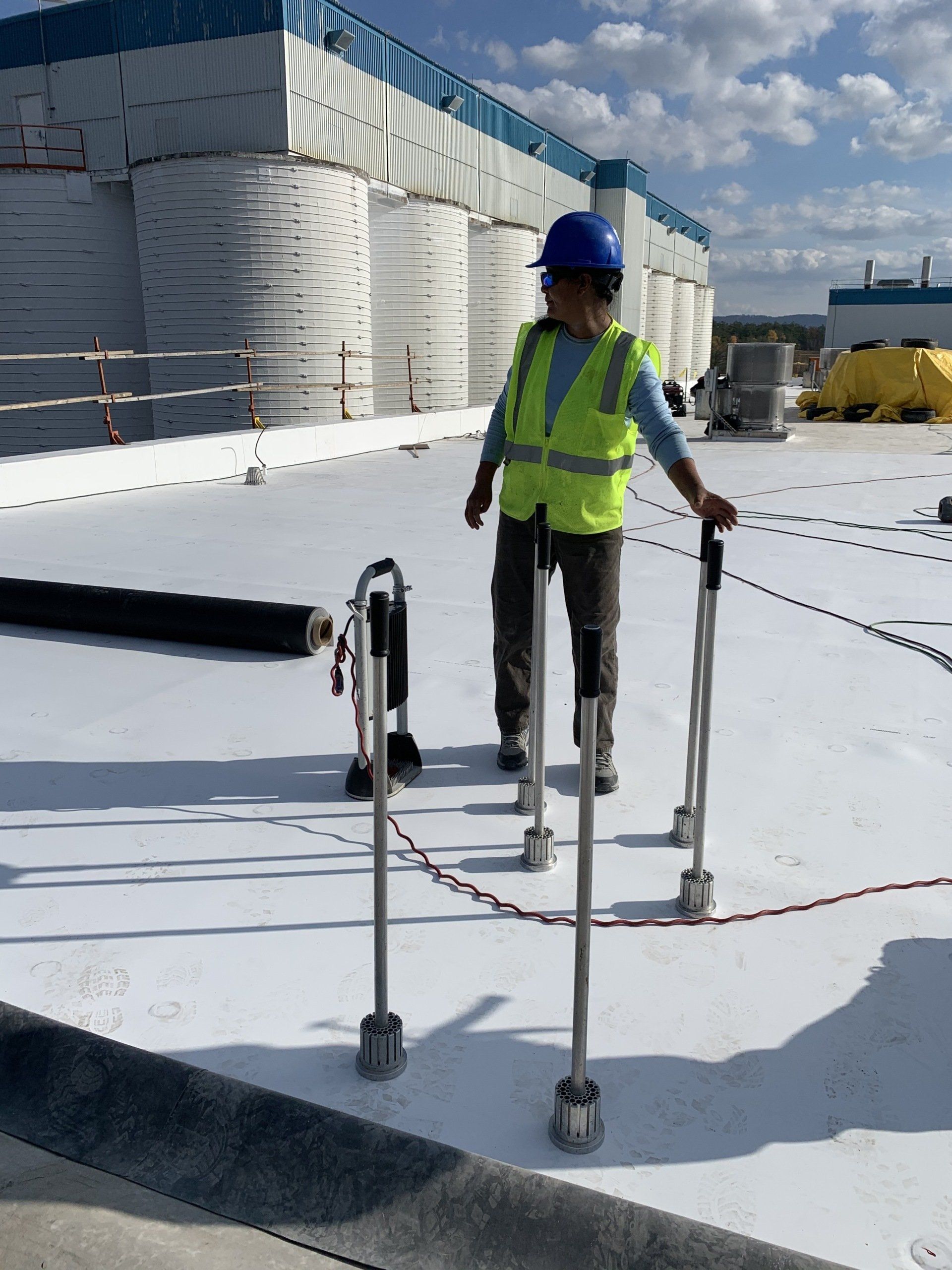 A man wearing a hard hat and safety vest is standing on a white roof