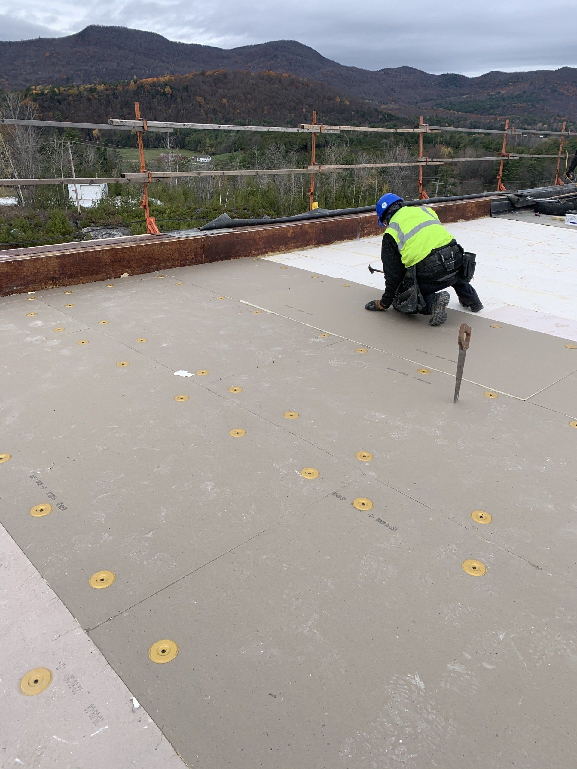 A construction worker is working on a roof with mountains in the background.