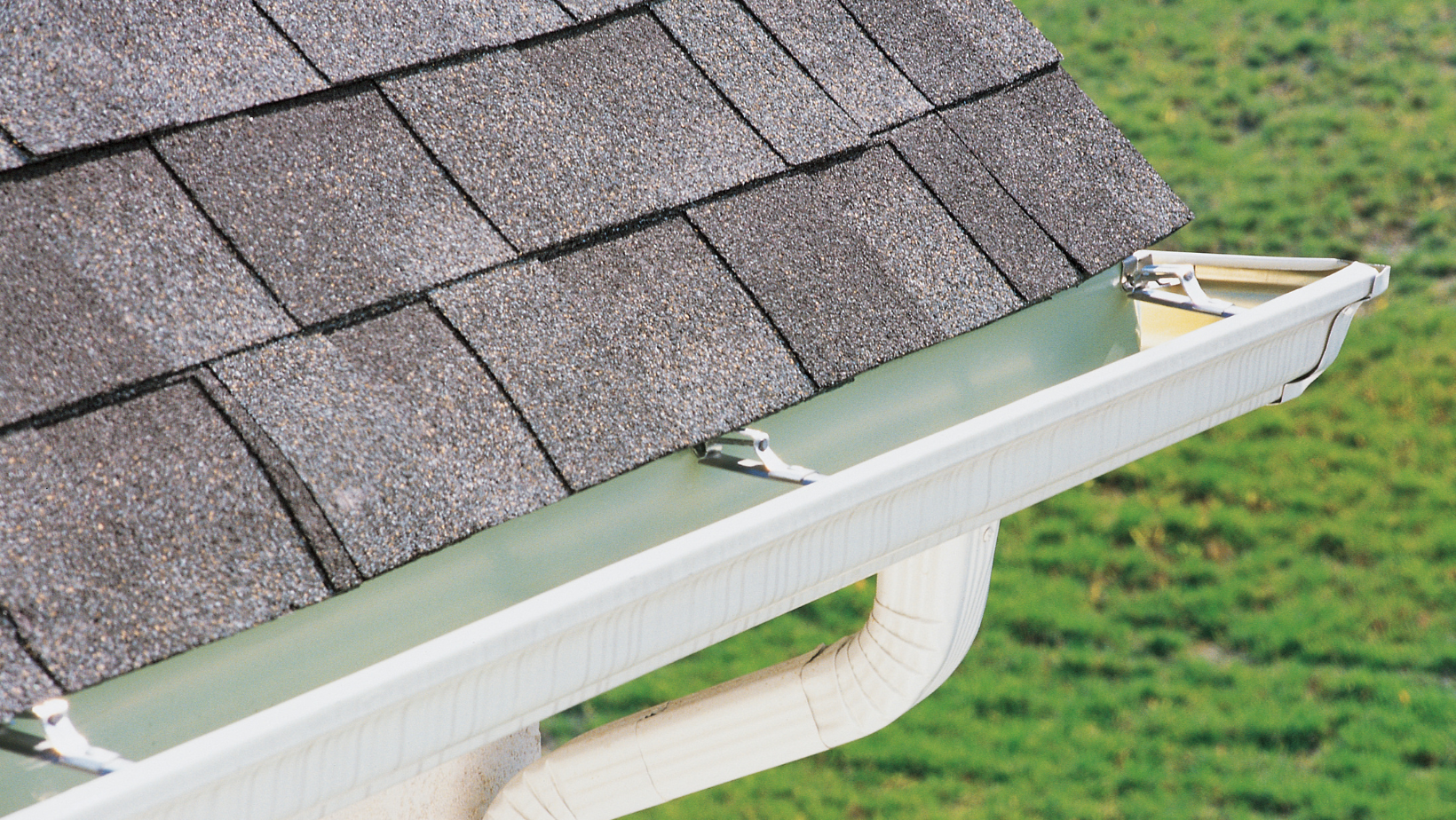 Rain gutter on a house with black shingles.