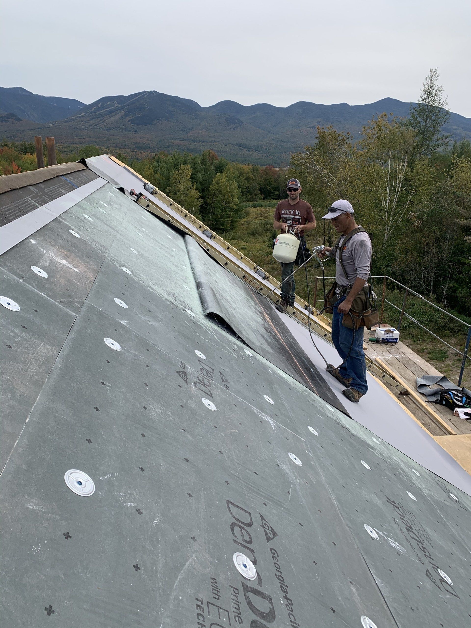 Two men are working on a roof with mountains in the background.