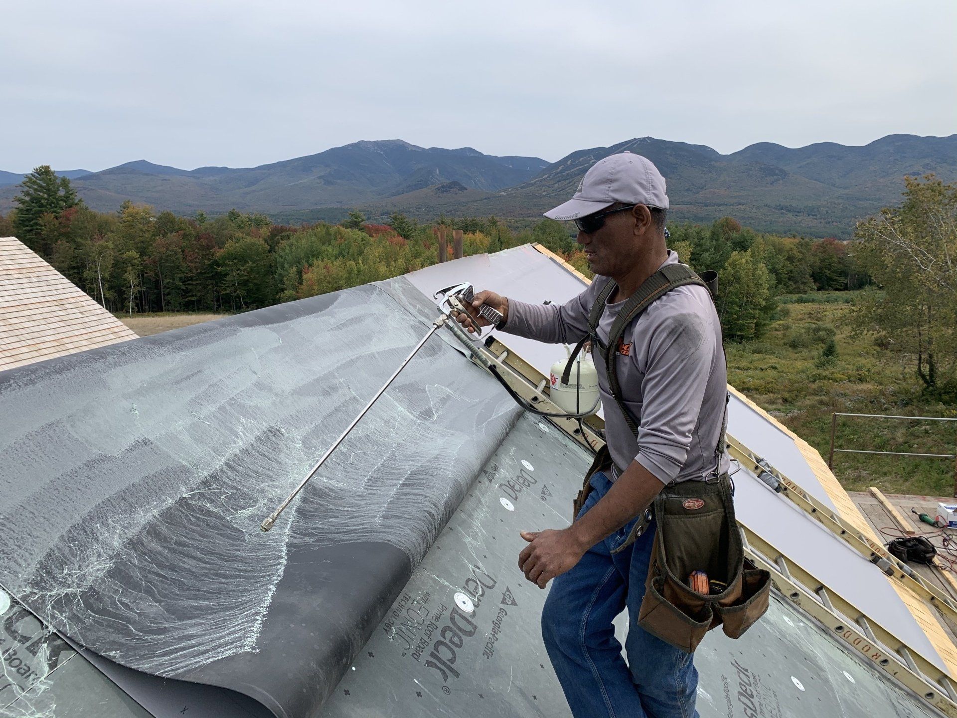 A man is working on a roof with mountains in the background.