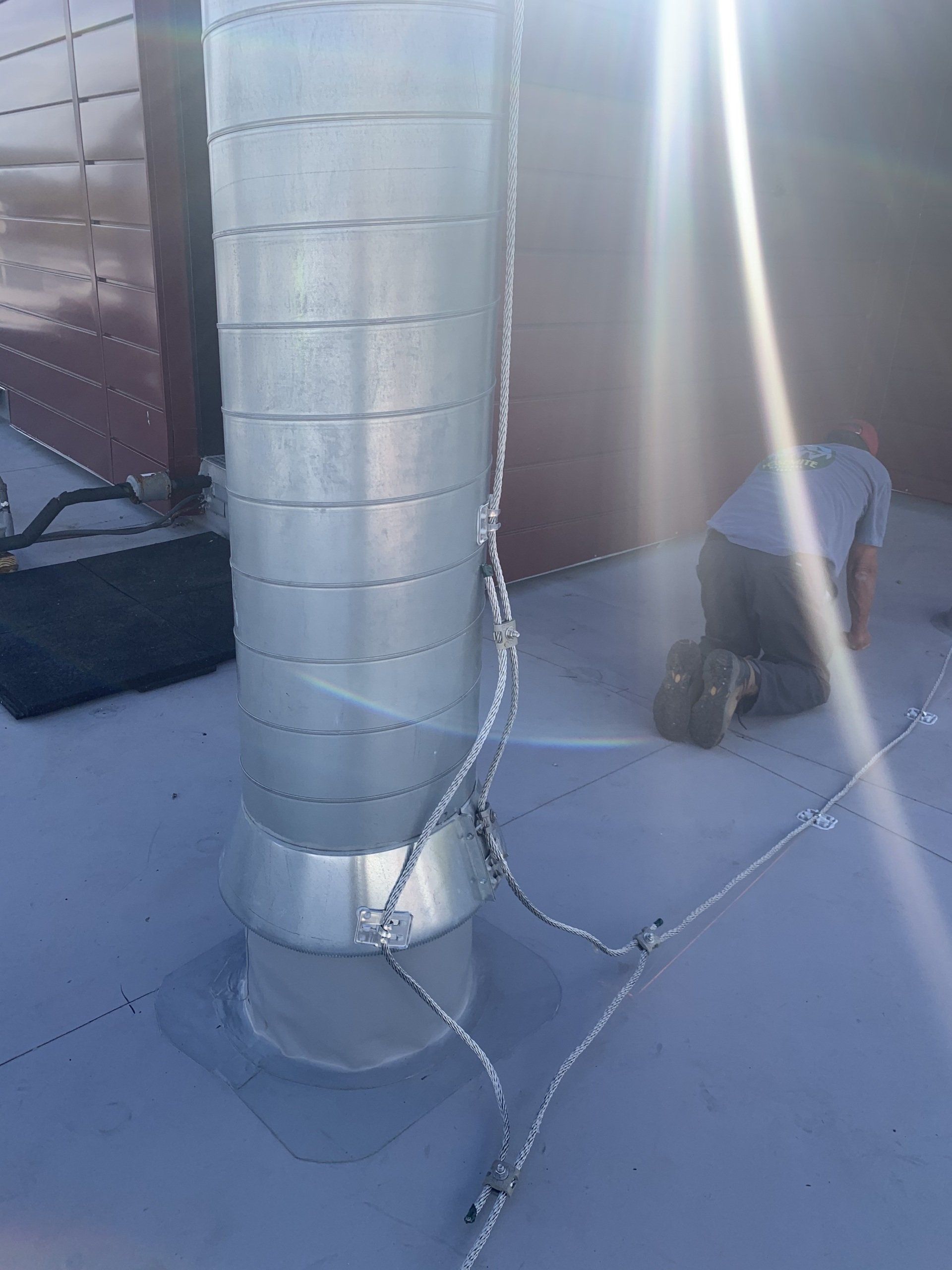 A man is kneeling down next to a metal pipe on a roof.