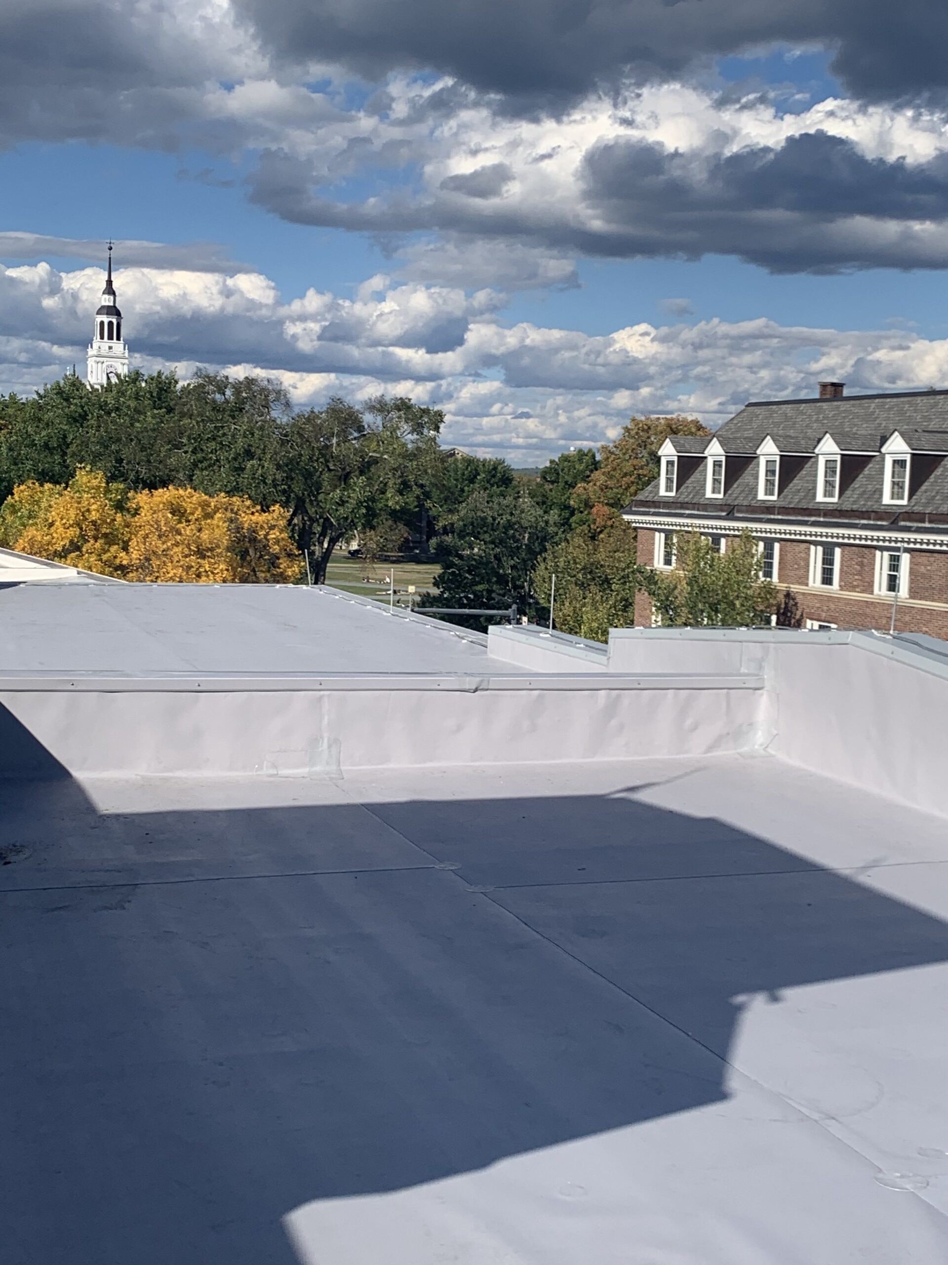 Rooftop with white parapet walls overlooking trees, brick buildings, and a cloudy blue sky