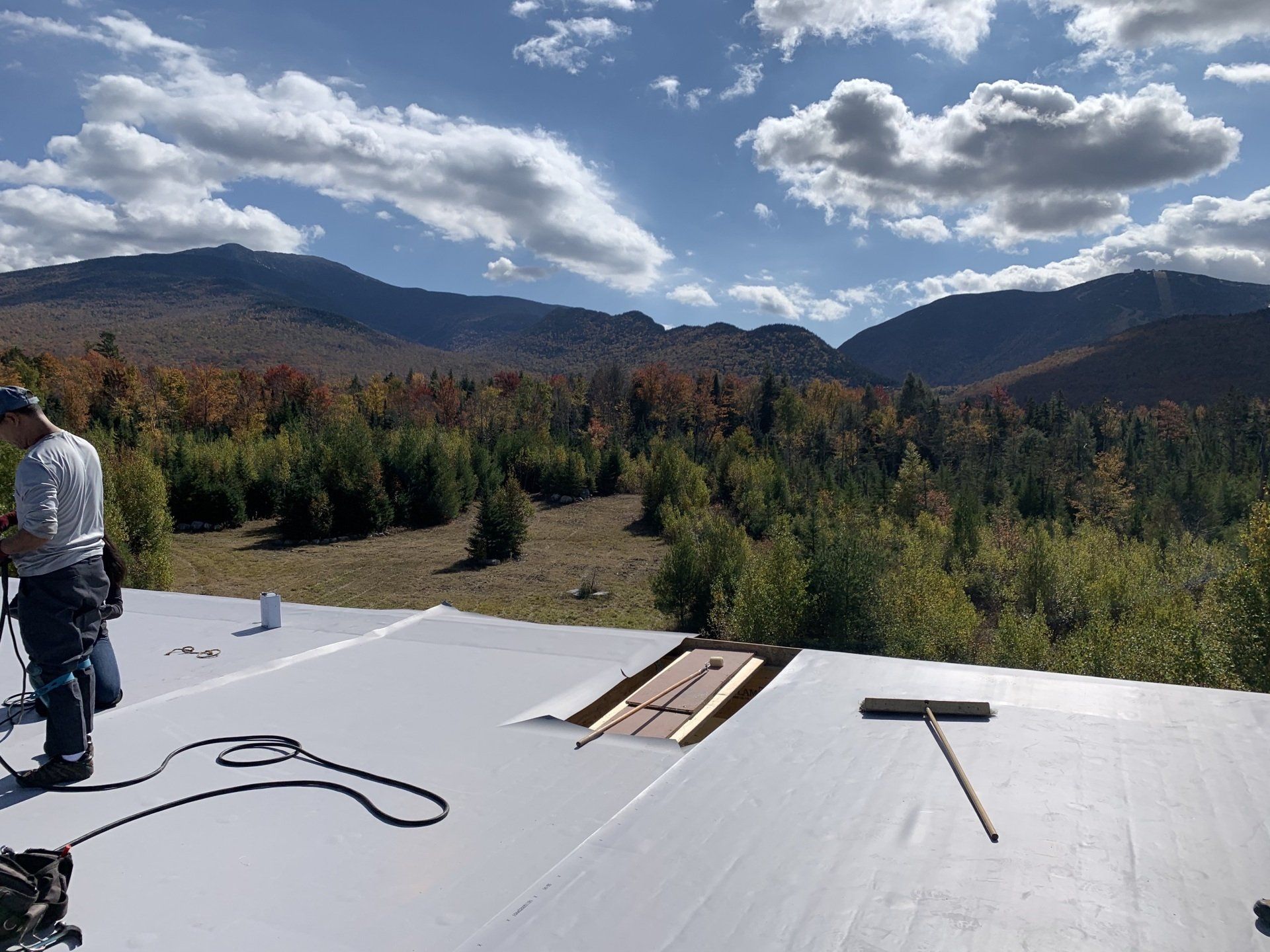 A man is working on a roof with mountains in the background.