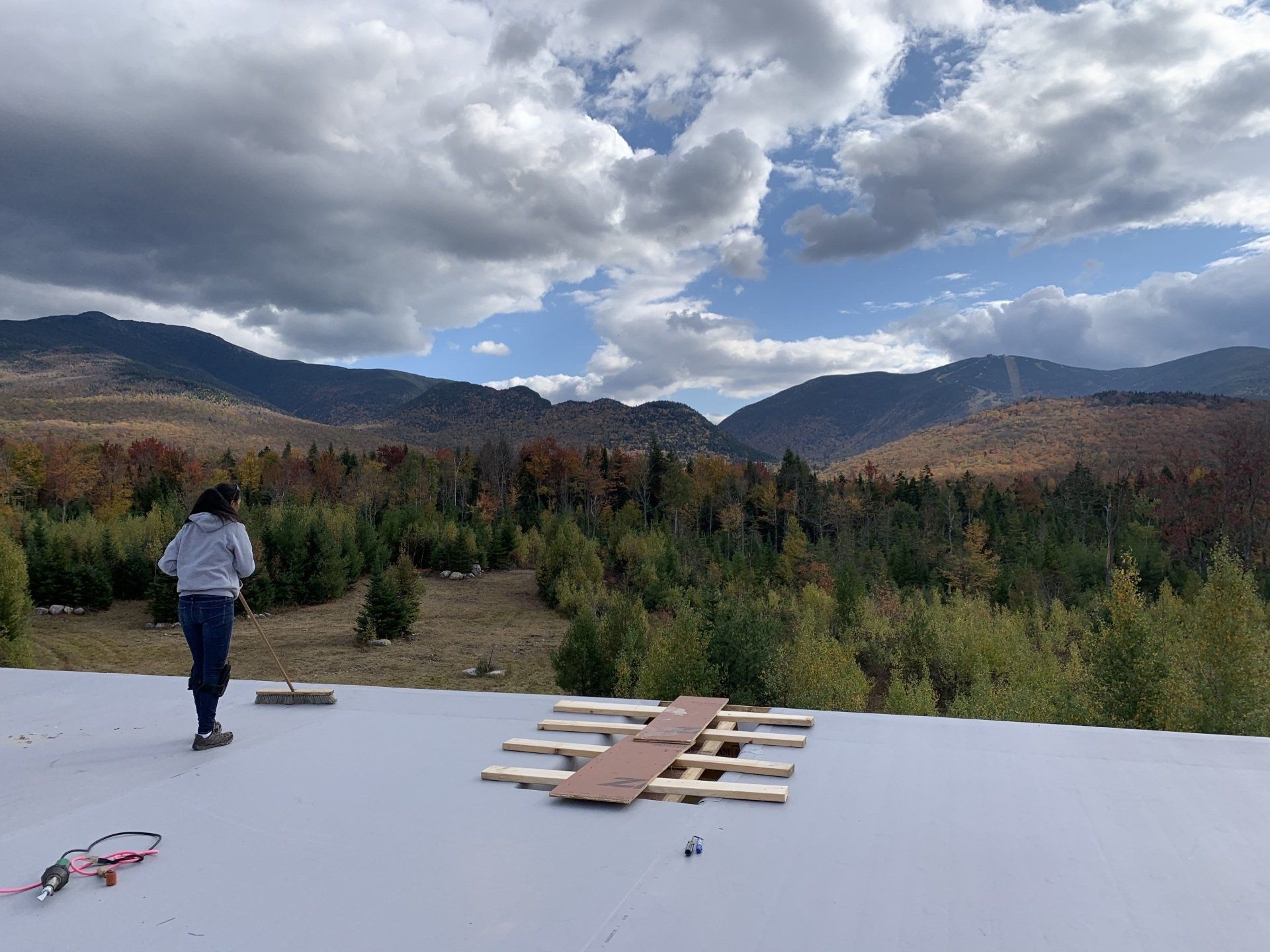 A person is standing on a roof overlooking a forest and mountains.