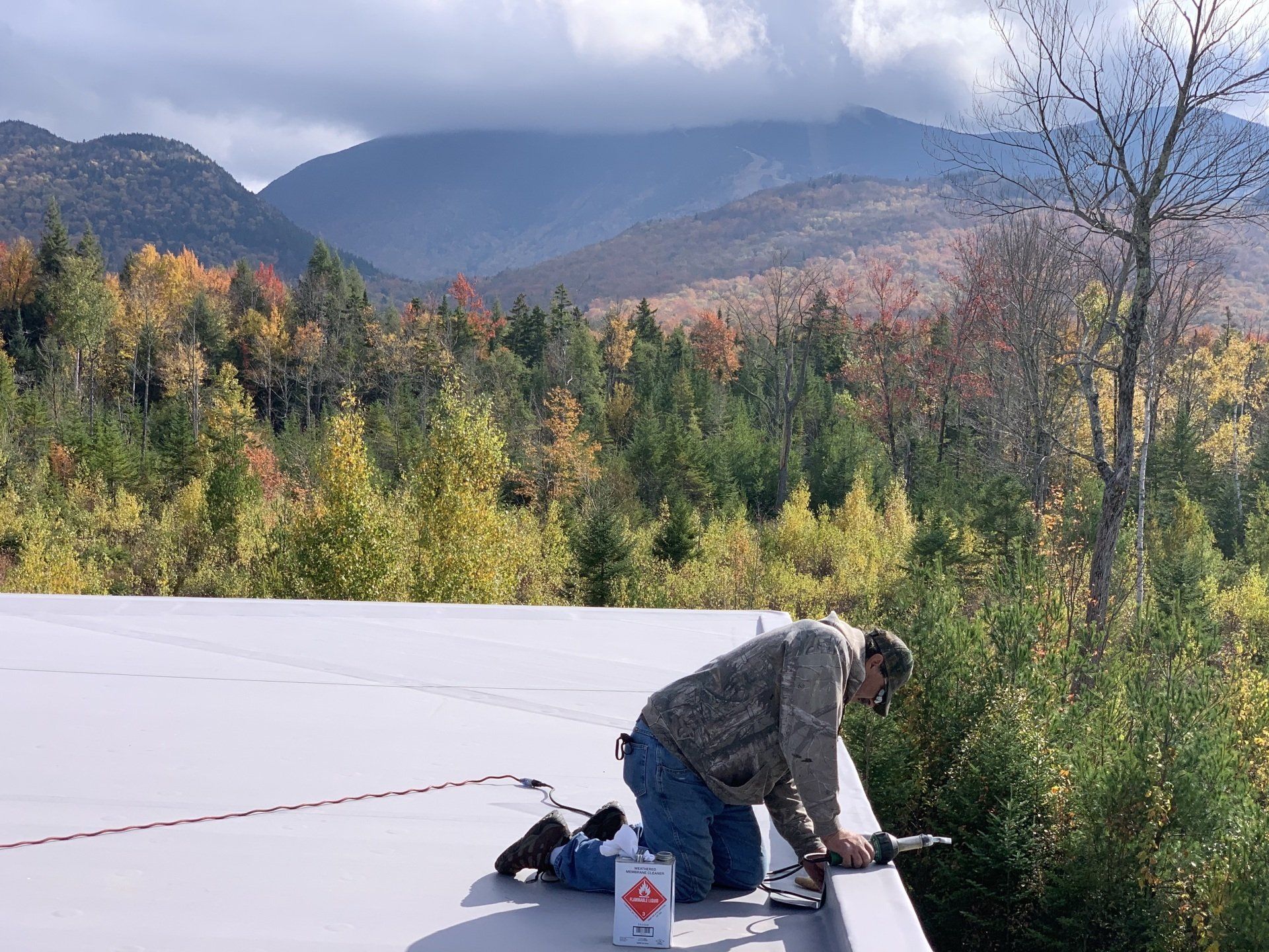 A man is working on a roof with mountains in the background.