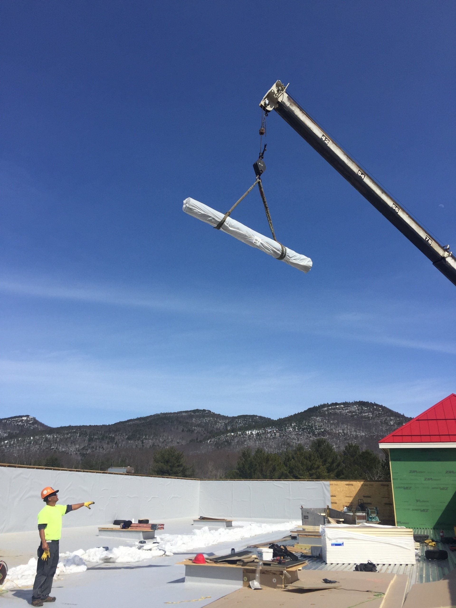 Rodd Roofing employees installing a new roof in New Hampshire using the crane