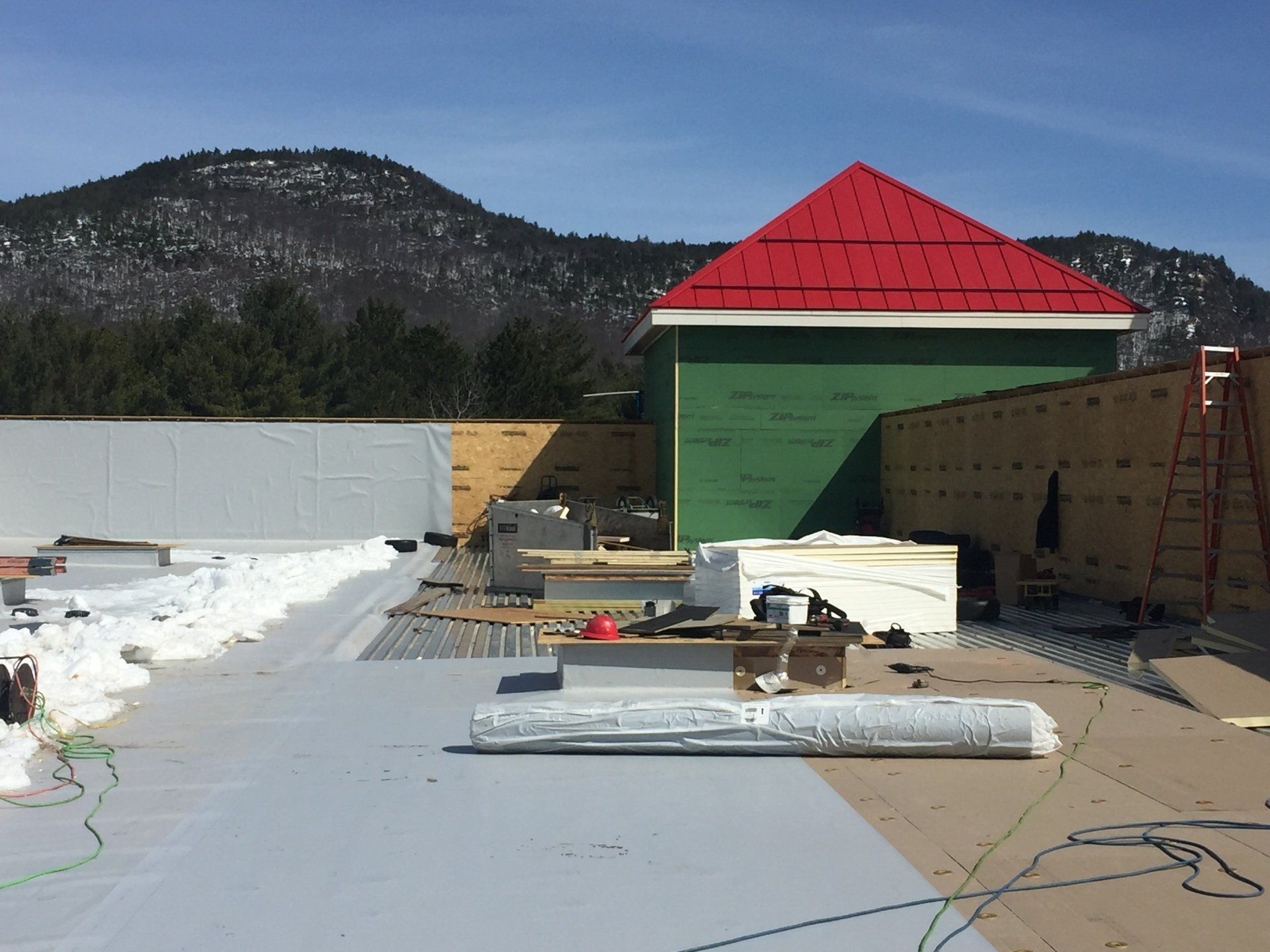 A building under construction with a red roof and mountains in the background