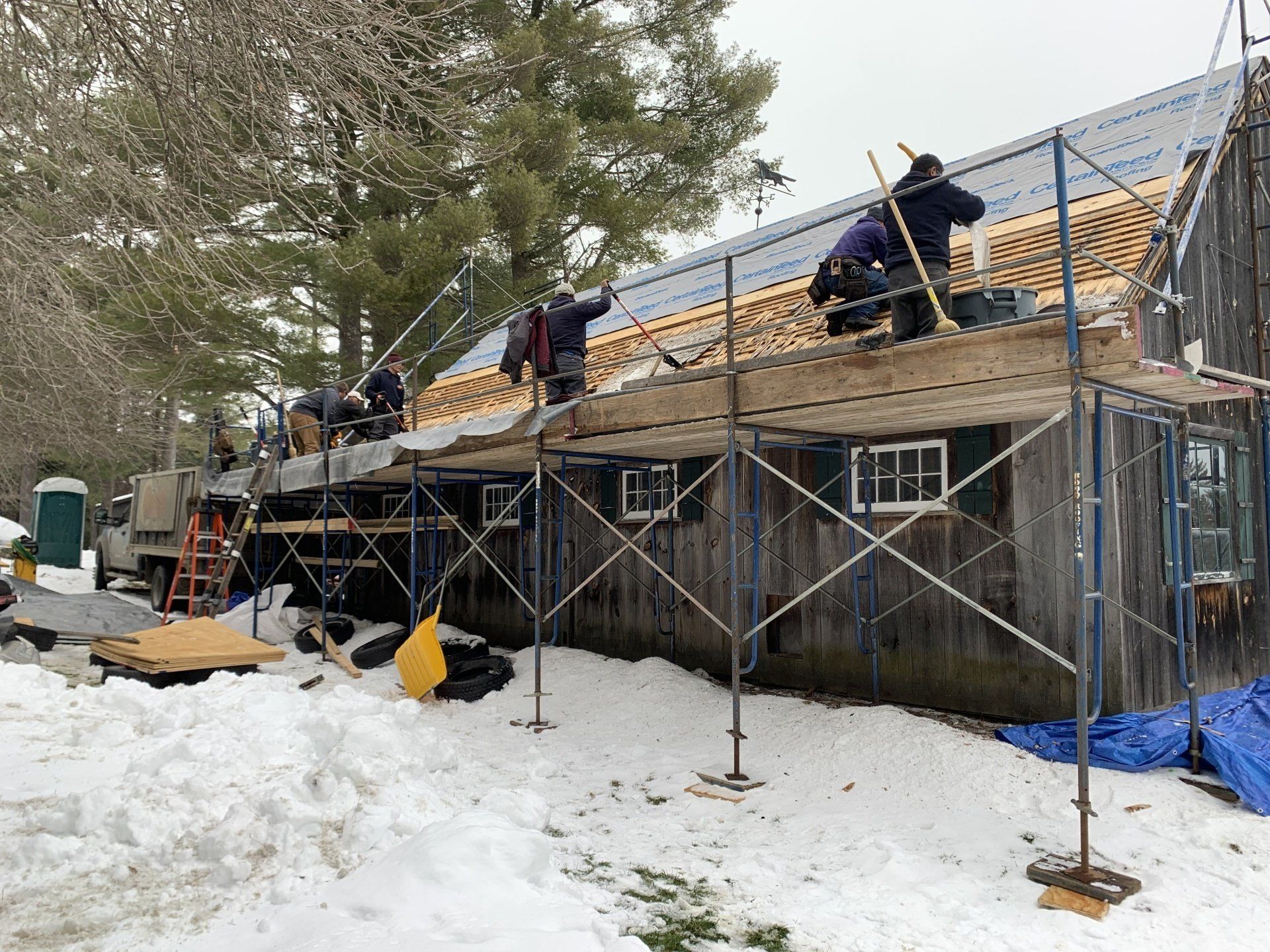 A group of men are working on the roof of a building in the snow.