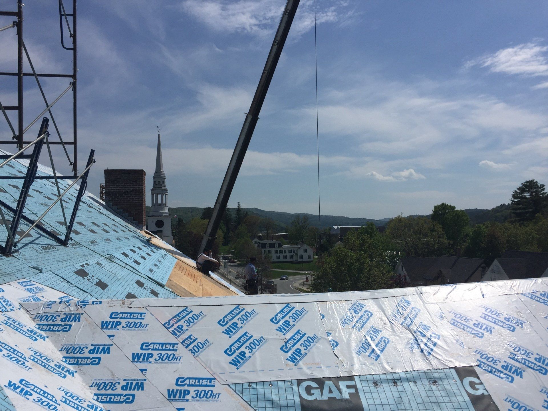A crane is lifting a piece of insulation on top of a roof