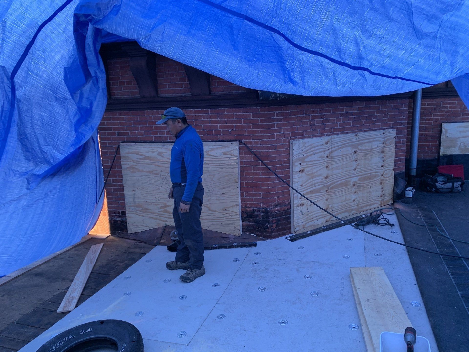 A Rodd Roofing employee standing under a section of roof tarped off to keep the repairs dry