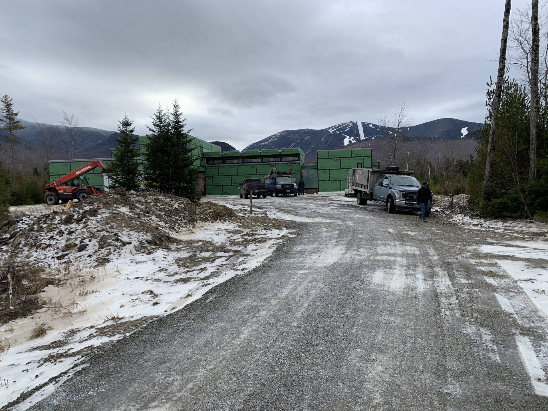 A snowy road leading to a building with mountains in the background.