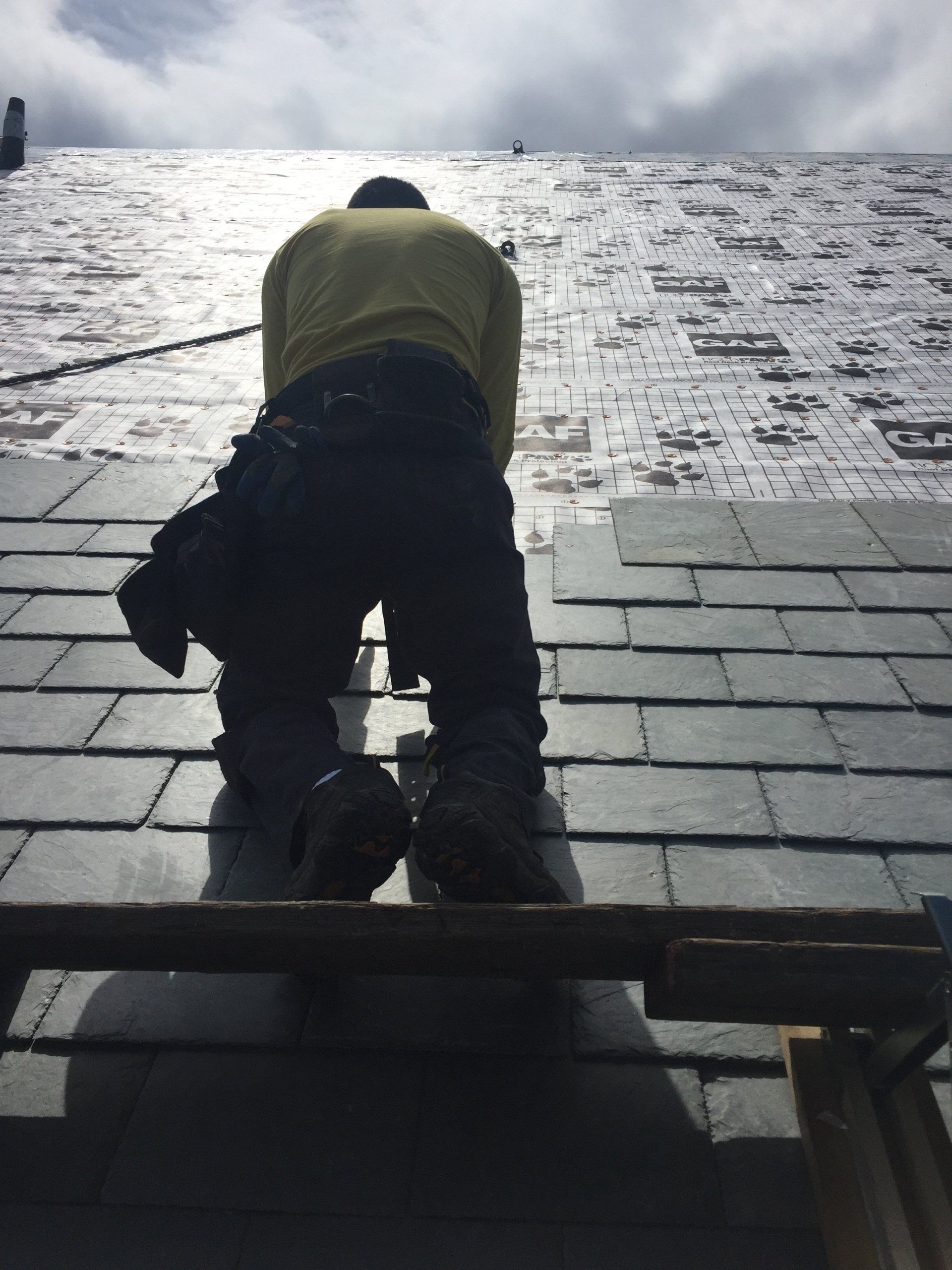 A man in a yellow shirt is kneeling on a roof