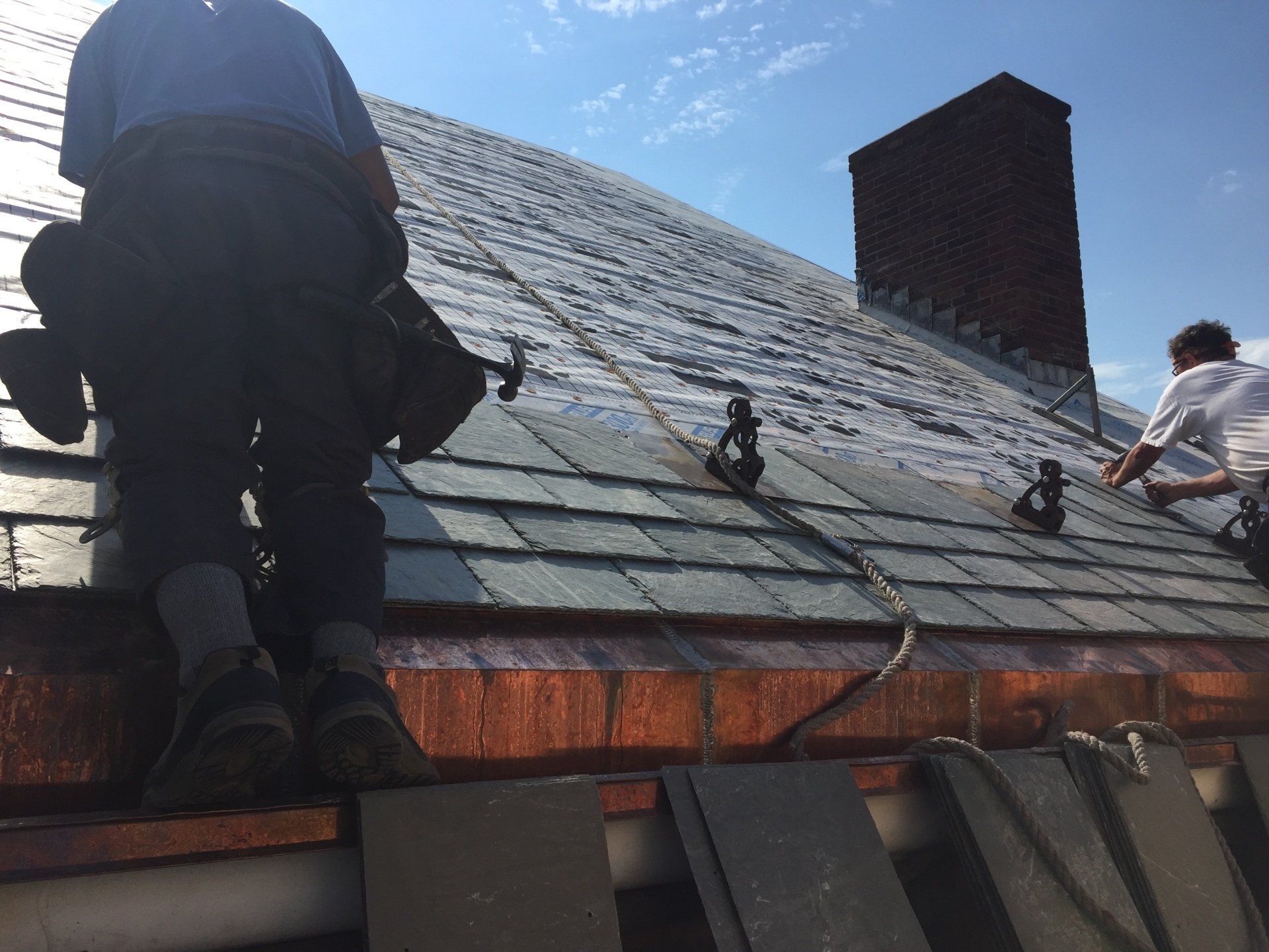 Two men are working on a roof with a chimney in the background