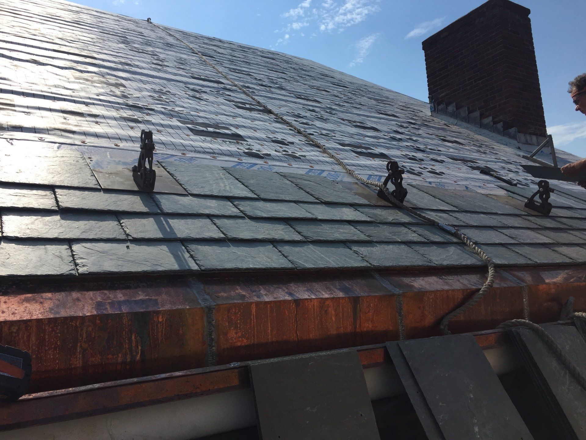 A person is working on a roof with a chimney in the background.