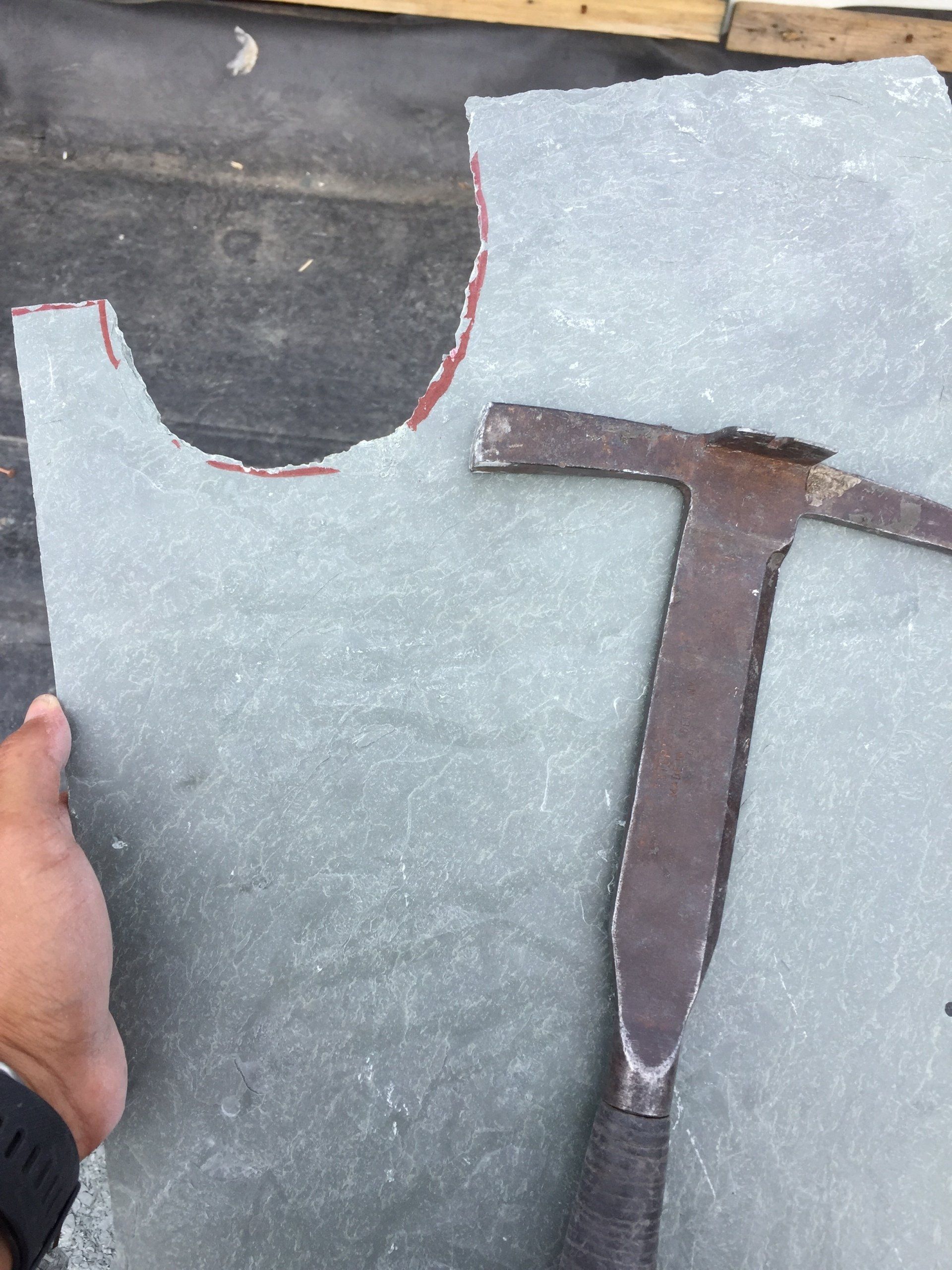 A person is holding a piece of slate next to a hammer
