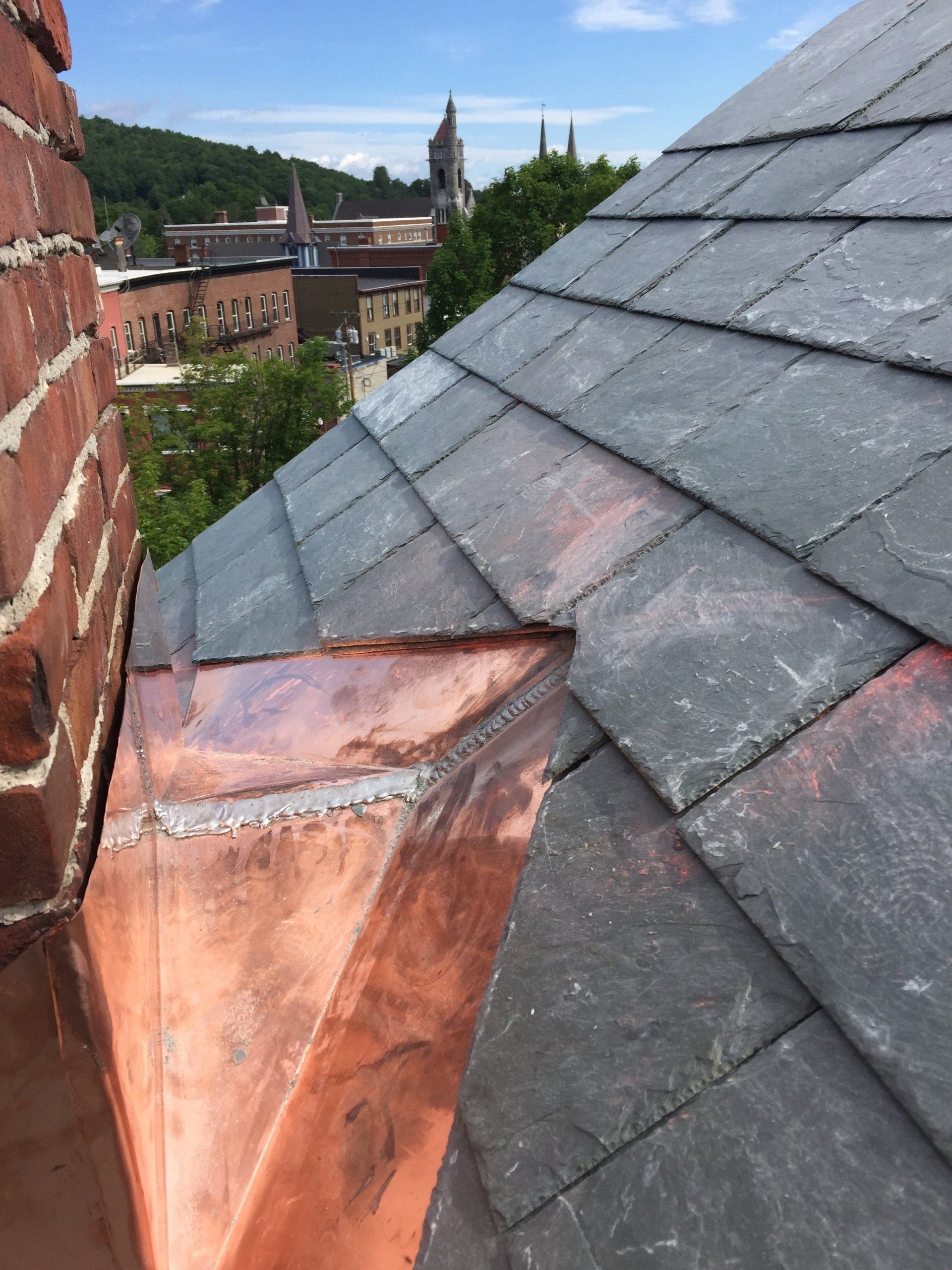 A close up of a roof with a copper gutter and slate tiles
