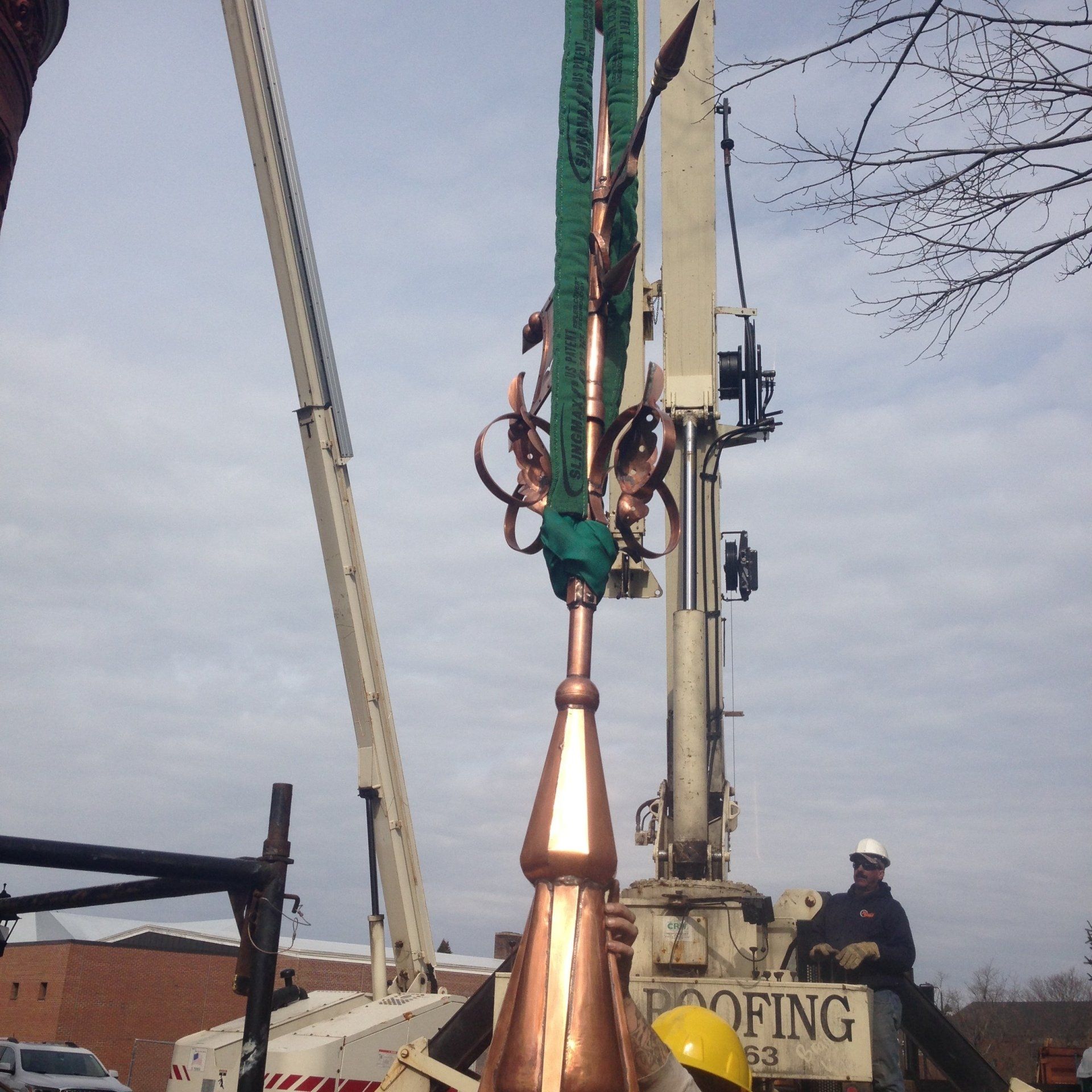 A roofing crane is lifting a large copper object