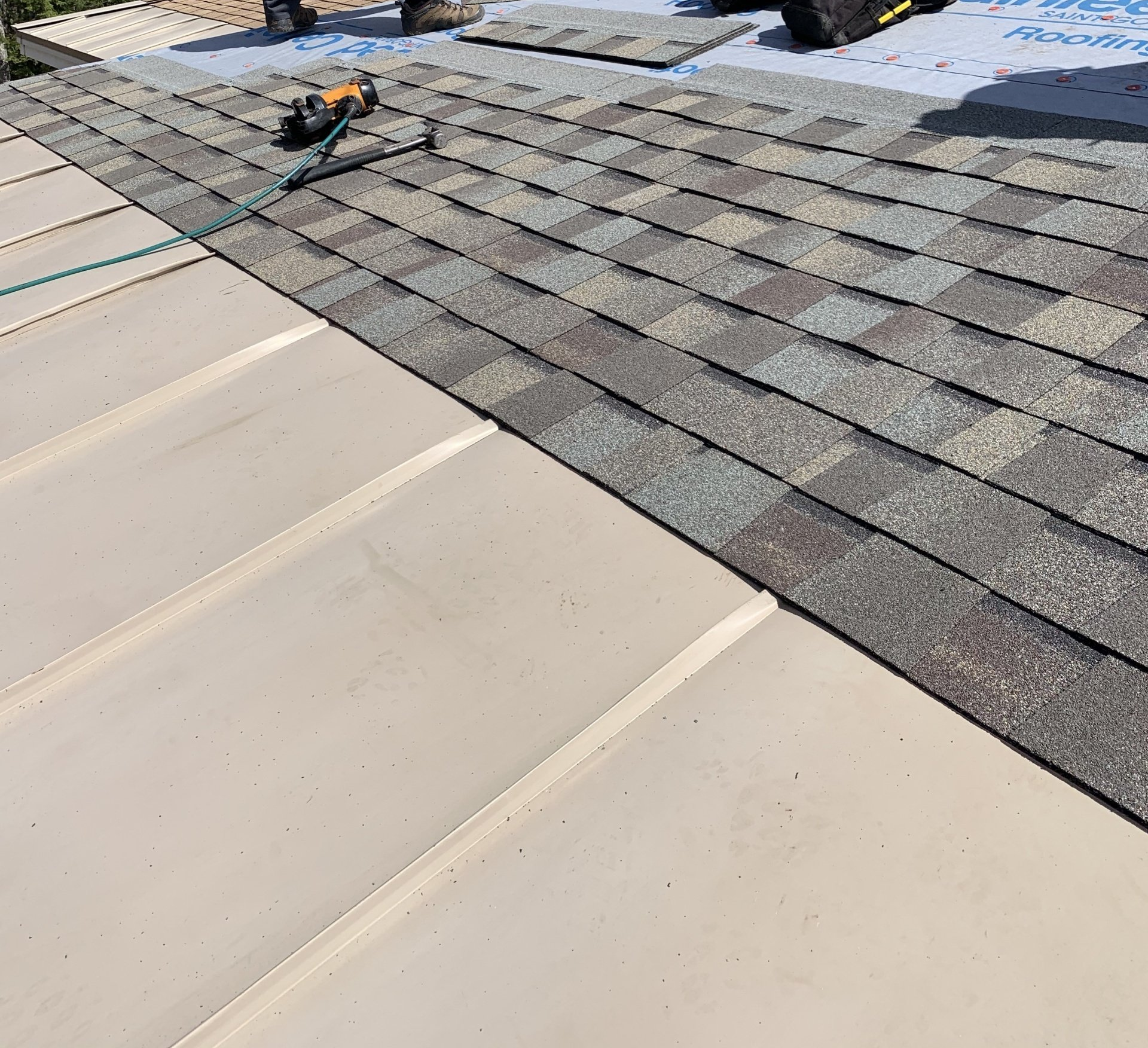 Roofing work on a house, with gray shingles meeting a light beige metal roof edge.
