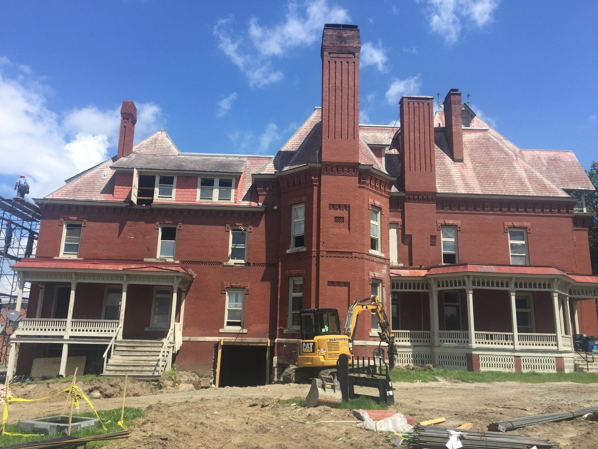 A large red brick house with a yellow excavator in front of it.
