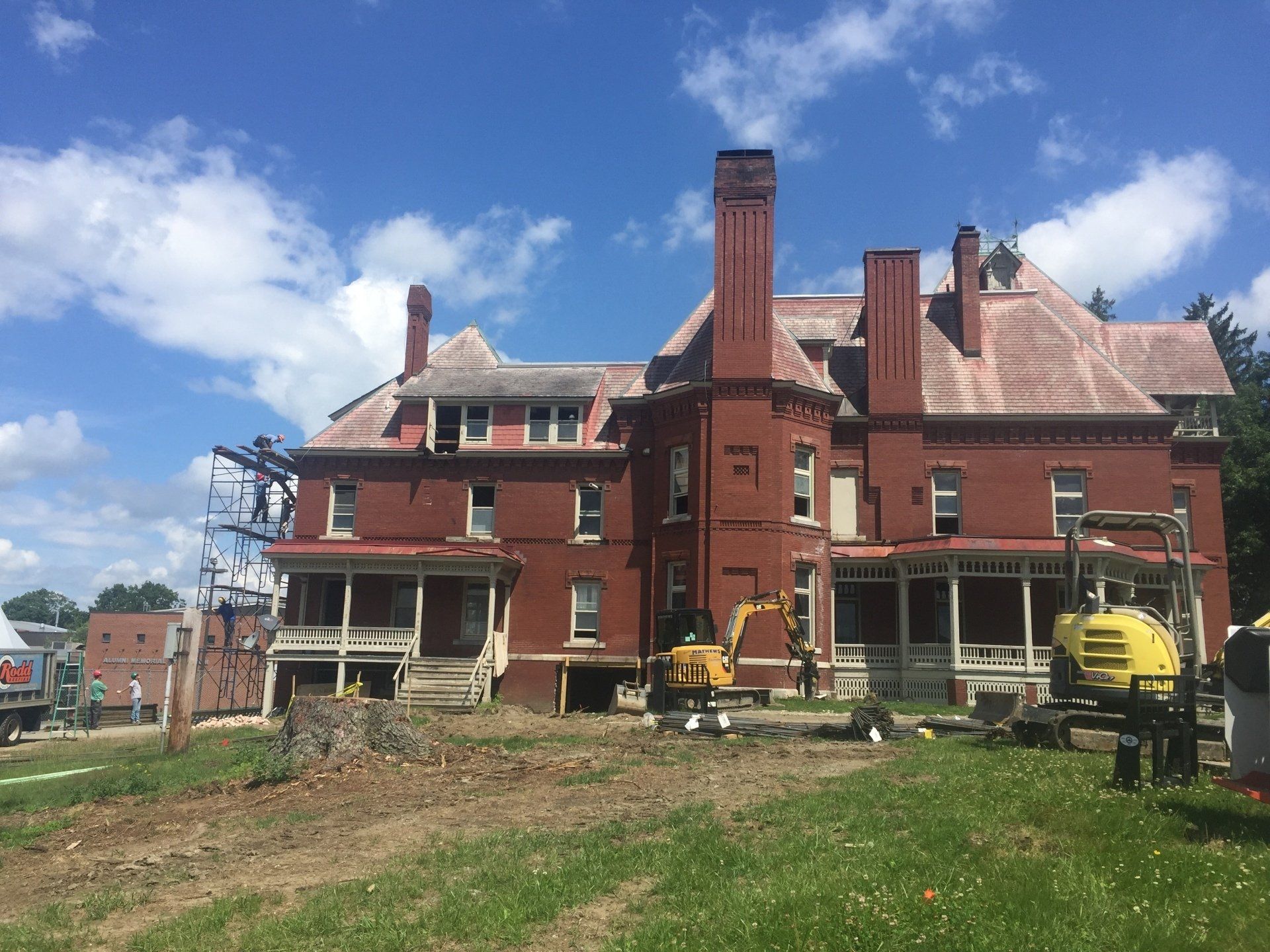 A large brick building is being demolished with a yellow excavator in front of it.