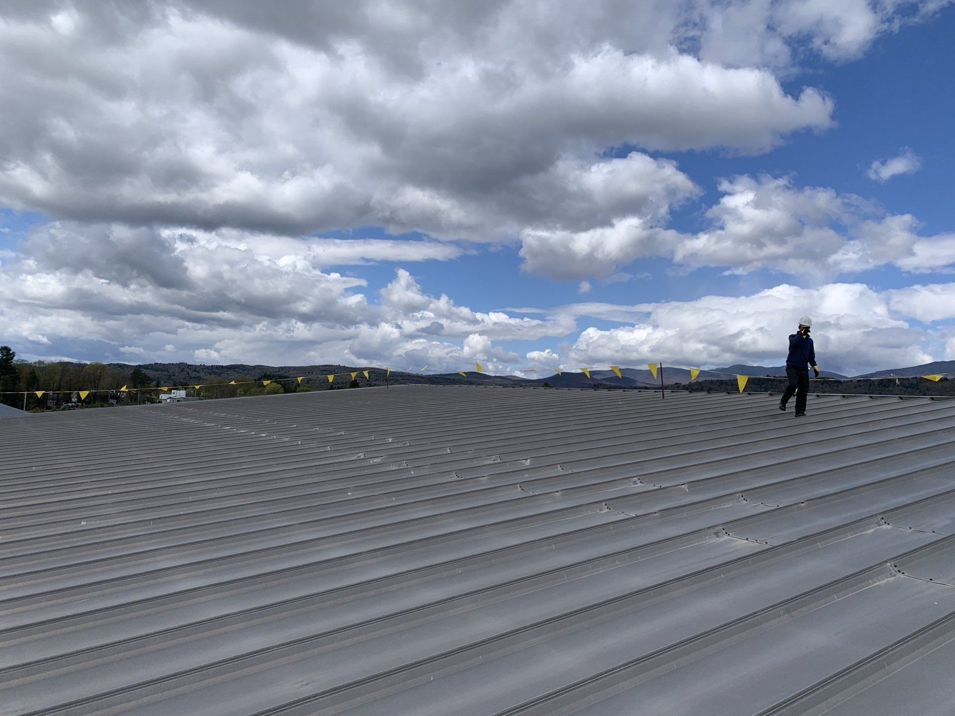 A man is standing on top of a roof with a blue sky in the background.