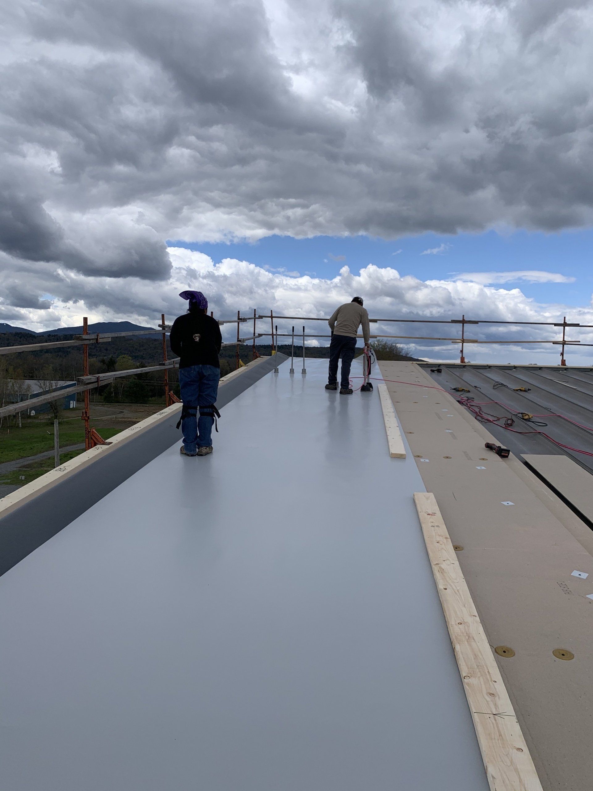 Two men are working on a roof with a cloudy sky in the background.