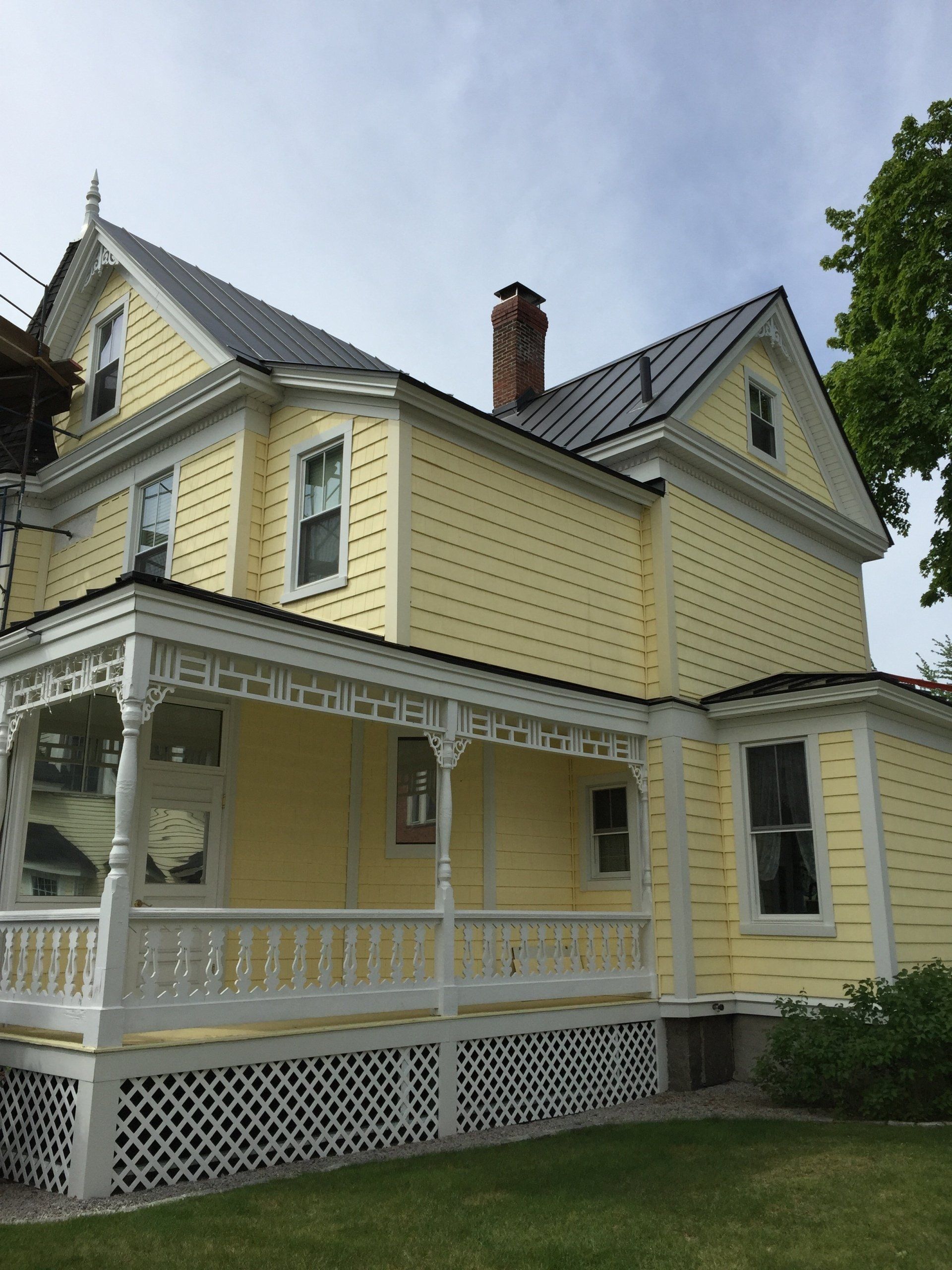 A yellow house with a white porch and a gray roof