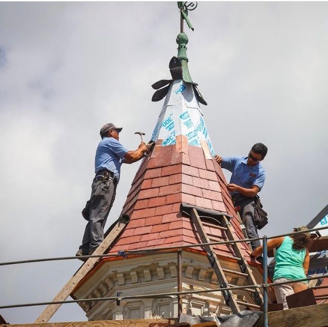 Two men are working on a roof with a weather vane on top