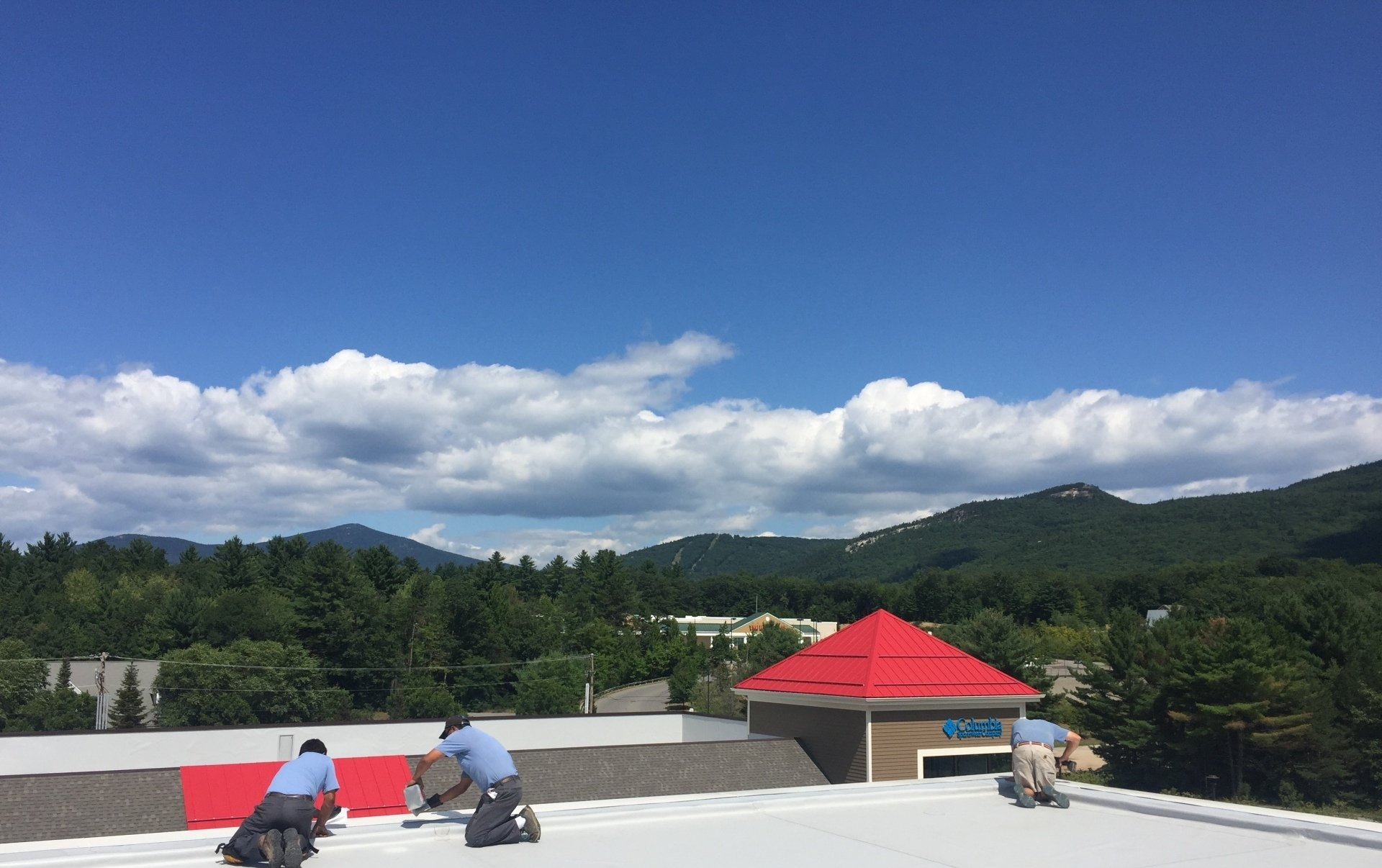 Rodd Roofing roofers are working on a roof in Vermont with mountains in the background.