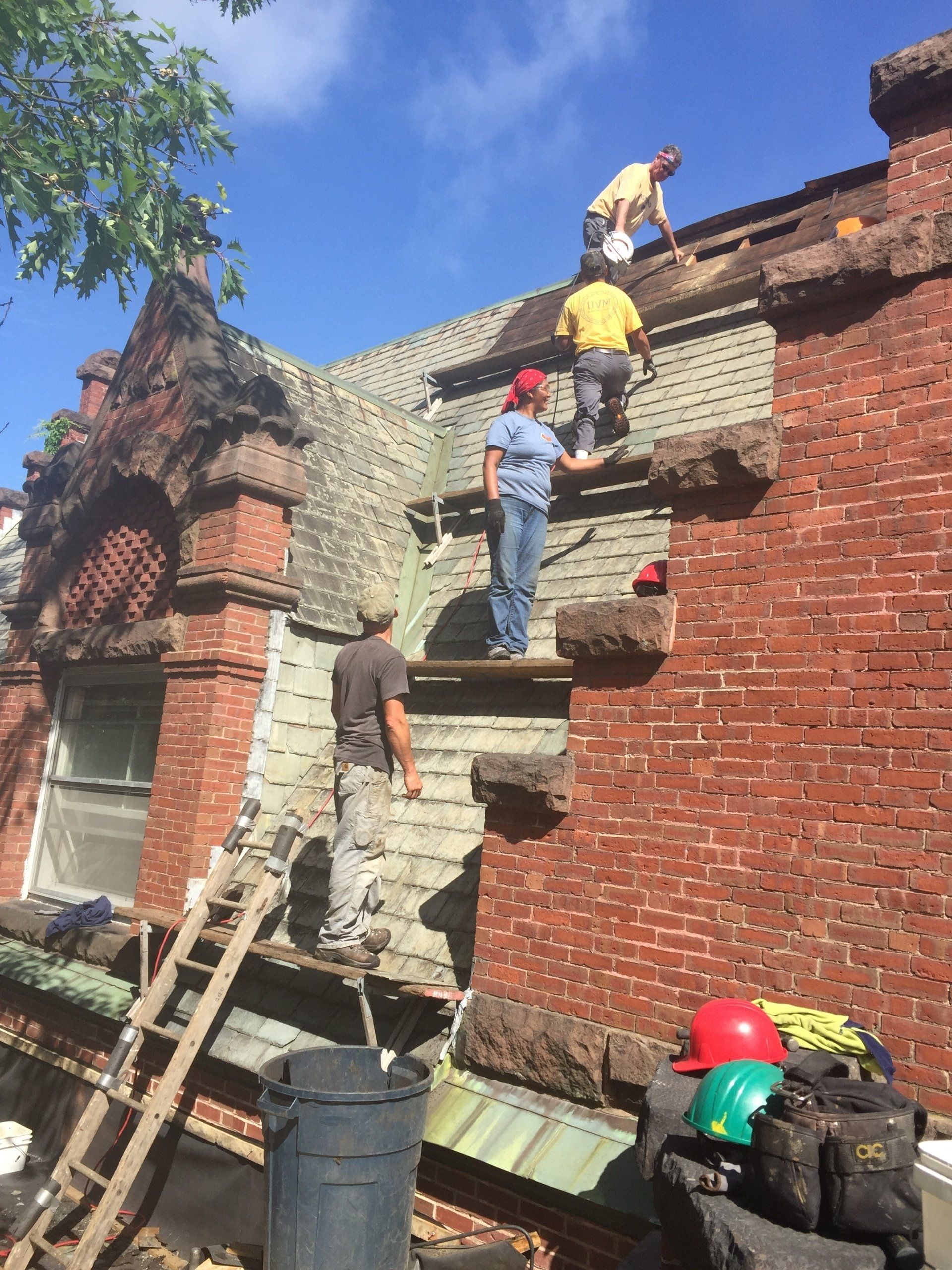 A group of people are working on the roof of a brick building.