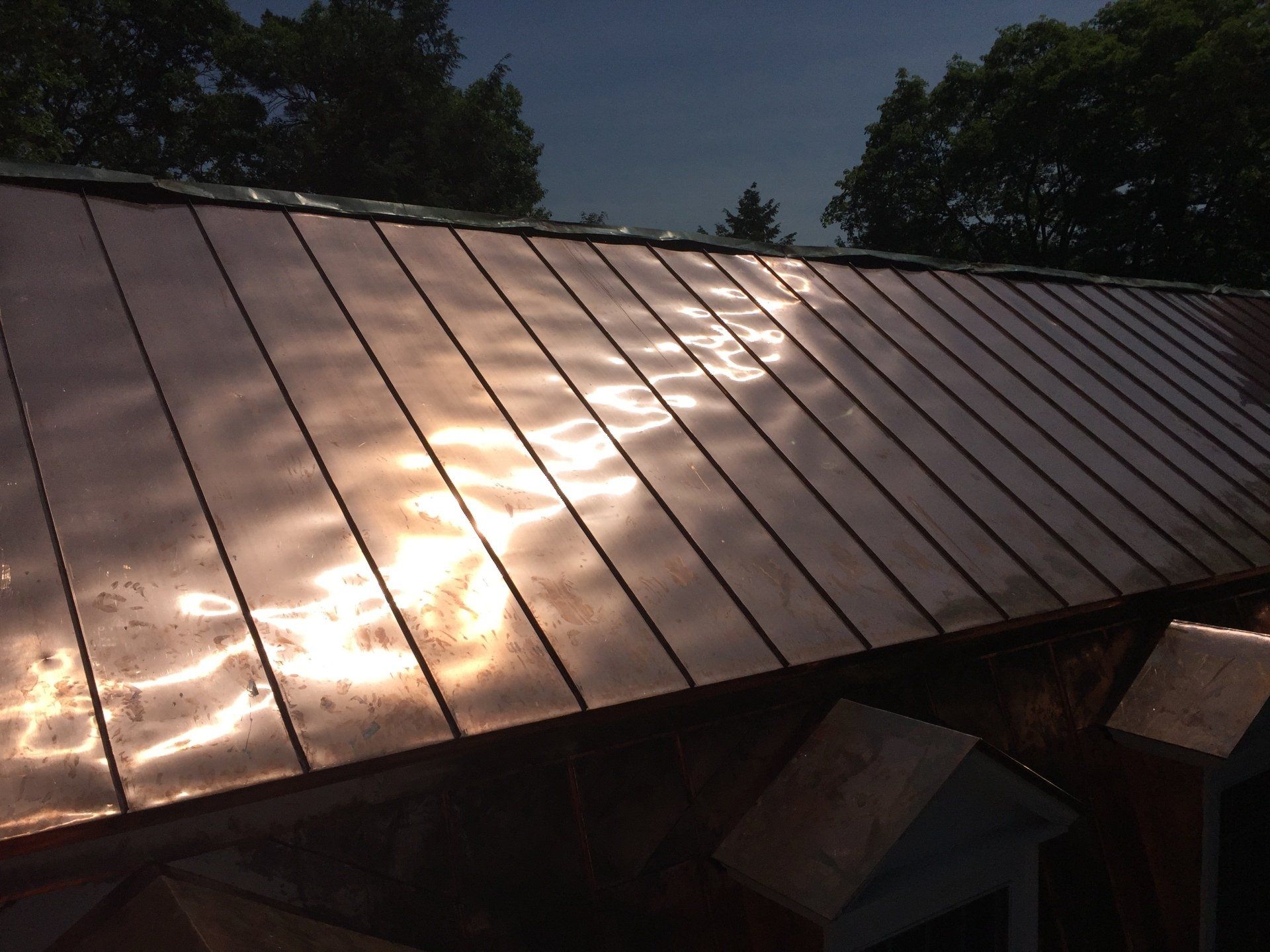 A close up of a copper roof with trees in the background