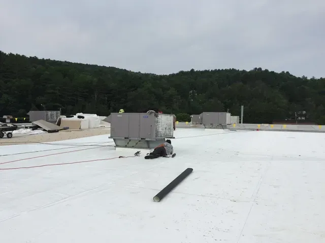 A Rodd Roofing roofing specialist laying on a Vermont roof next to the HVAC system inspecting it