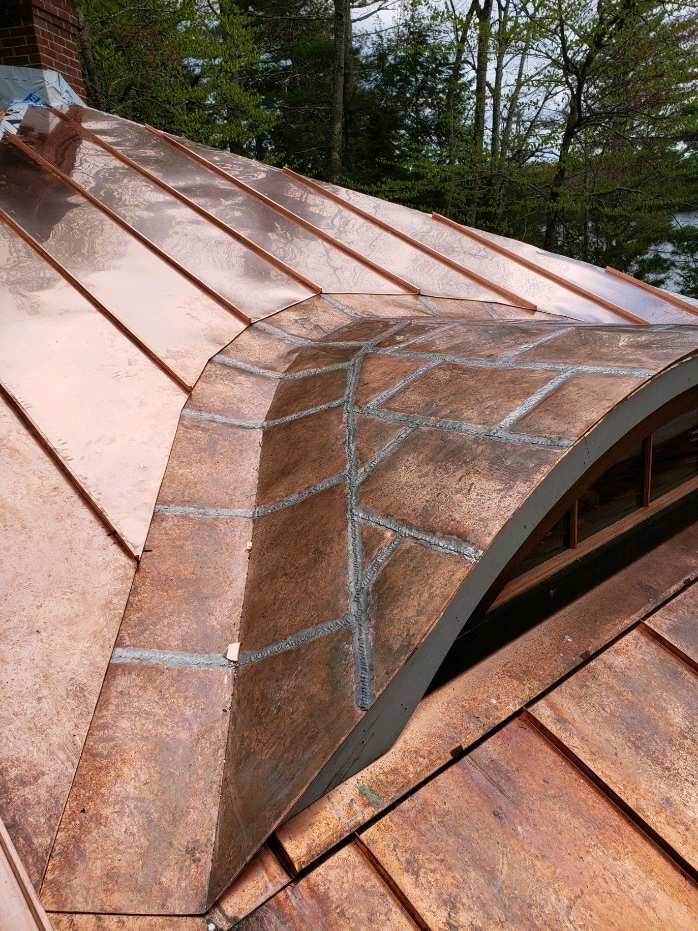 A close up of a copper roof with trees in the background
