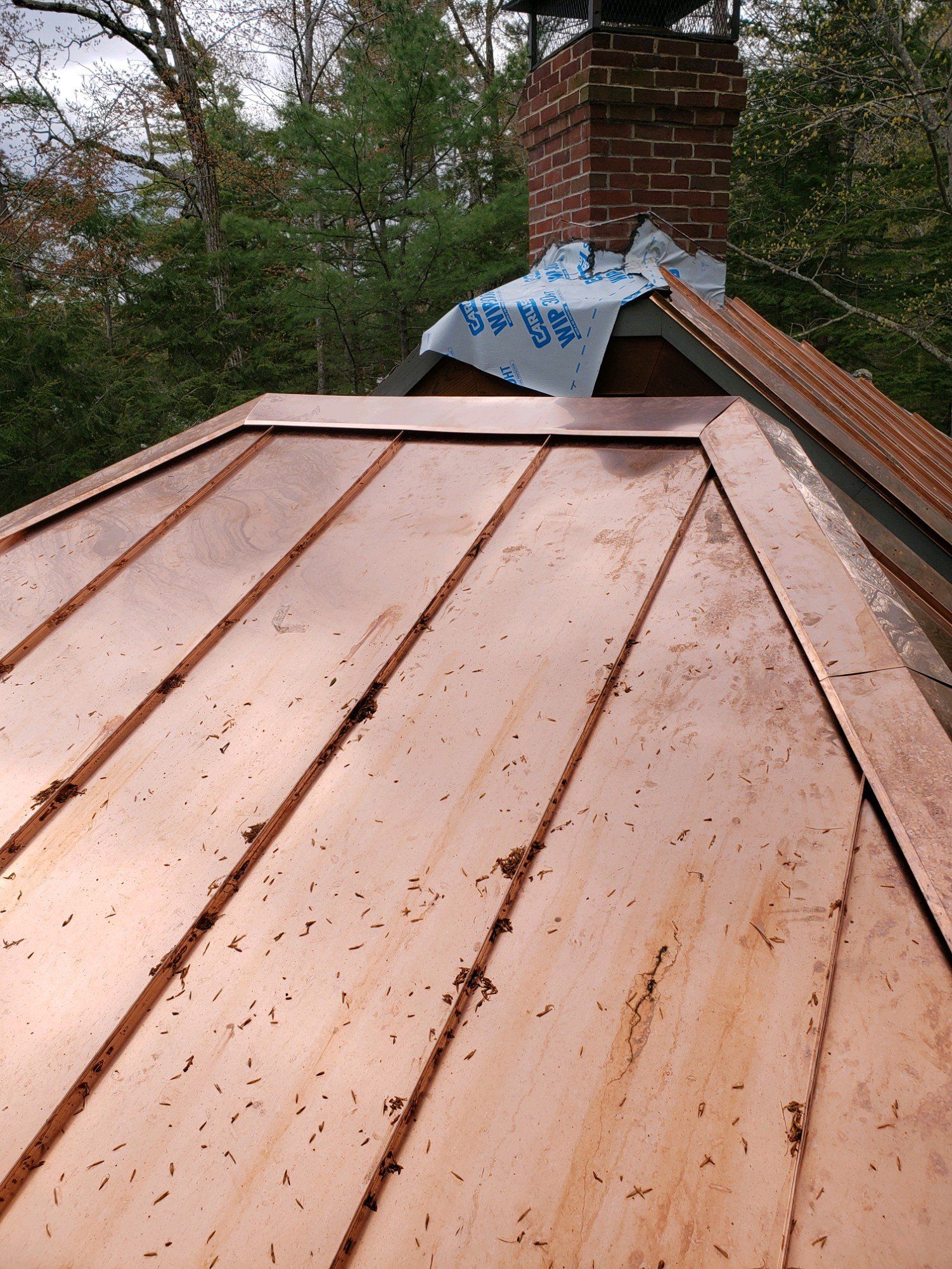 A close up of a copper roof with a chimney in the background