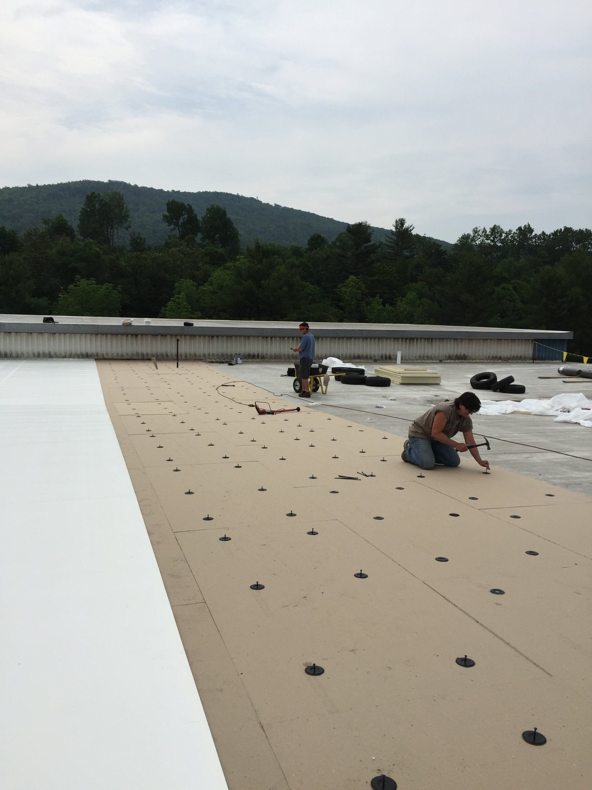 Two men are working on a roof with mountains in the background