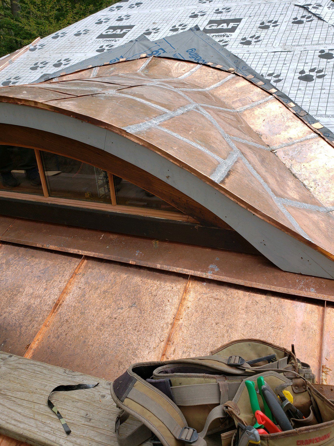 A tool bag is sitting on top of a copper roof.