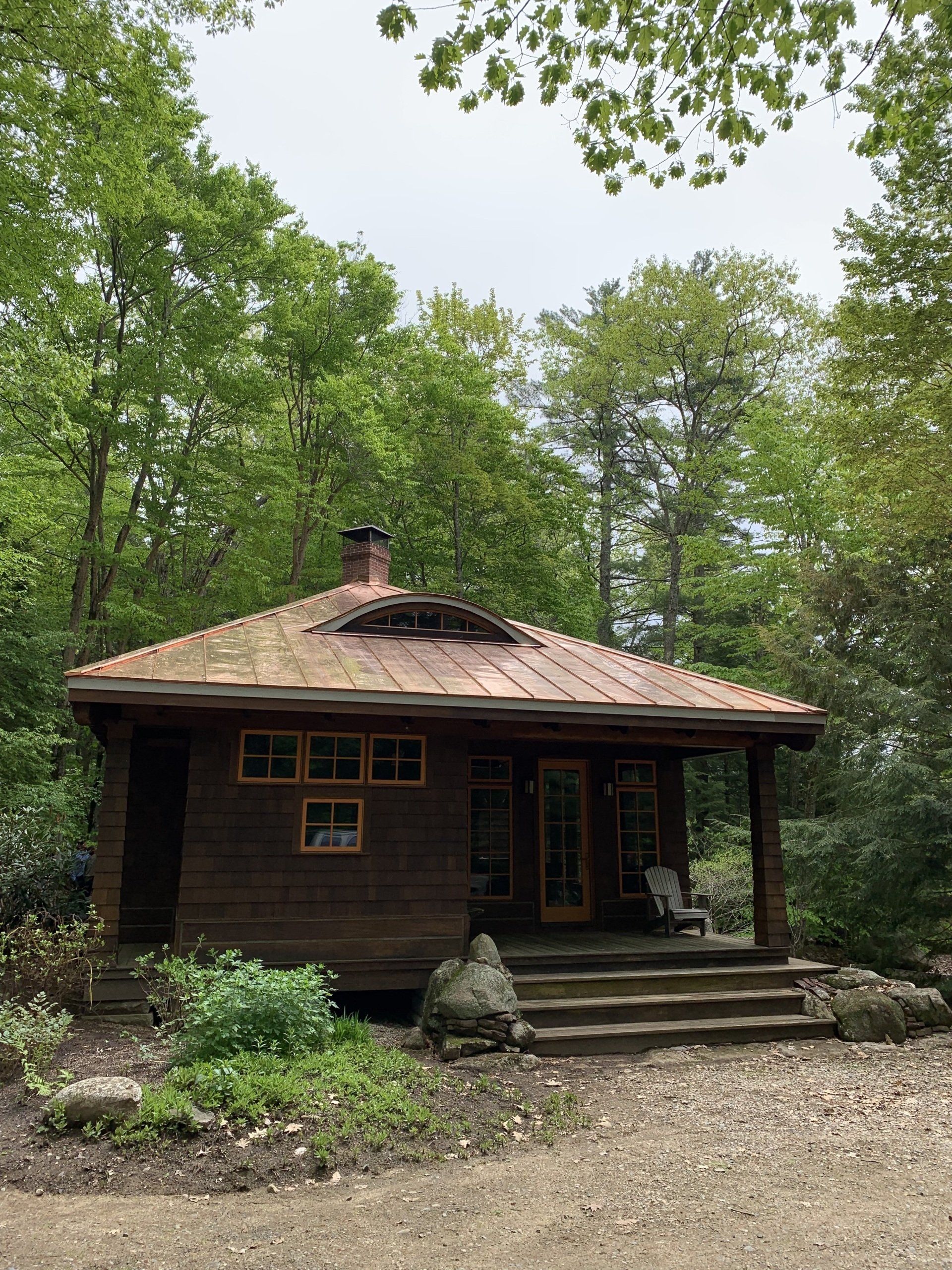 A small wooden house with a copper roof is surrounded by trees.