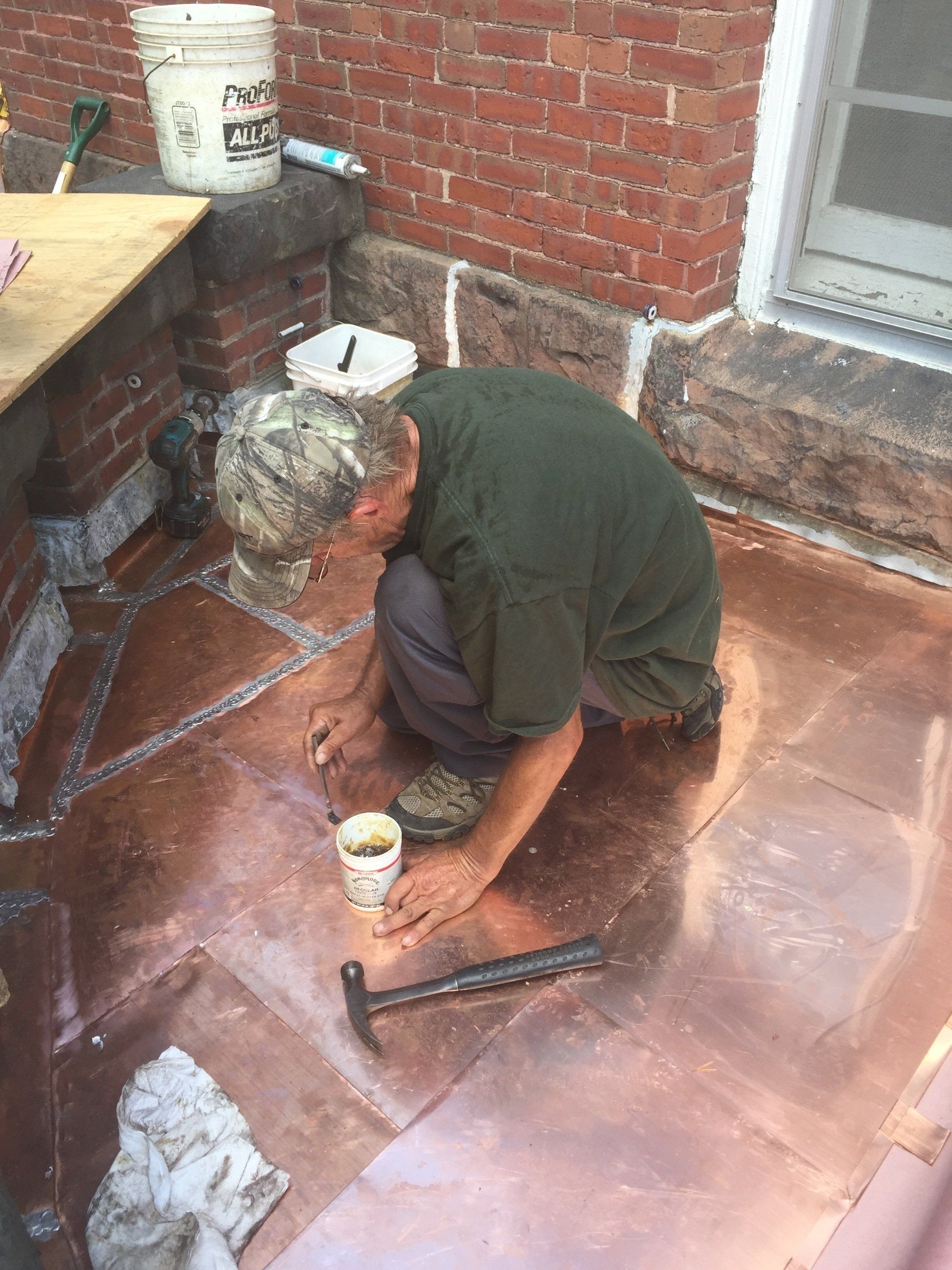 A man is working on a copper roof with a hammer.