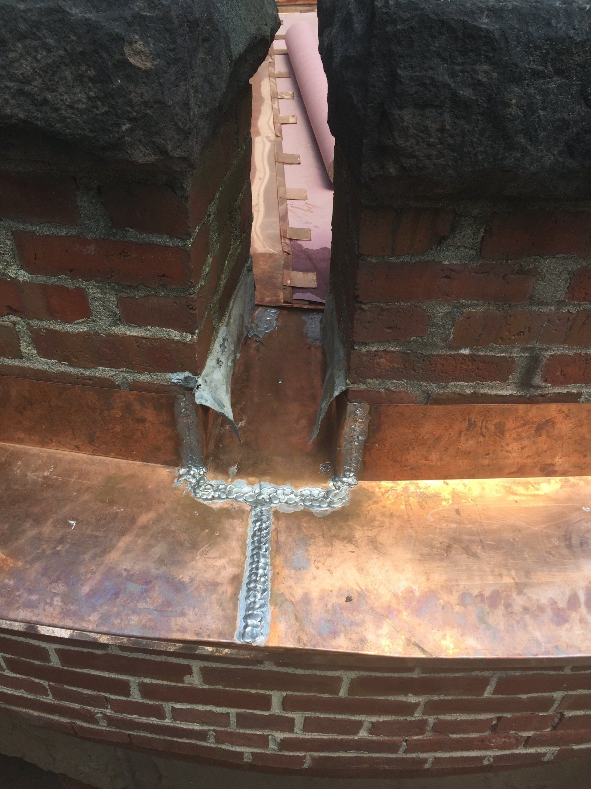 A brick wall with a copper gutter between two bricks