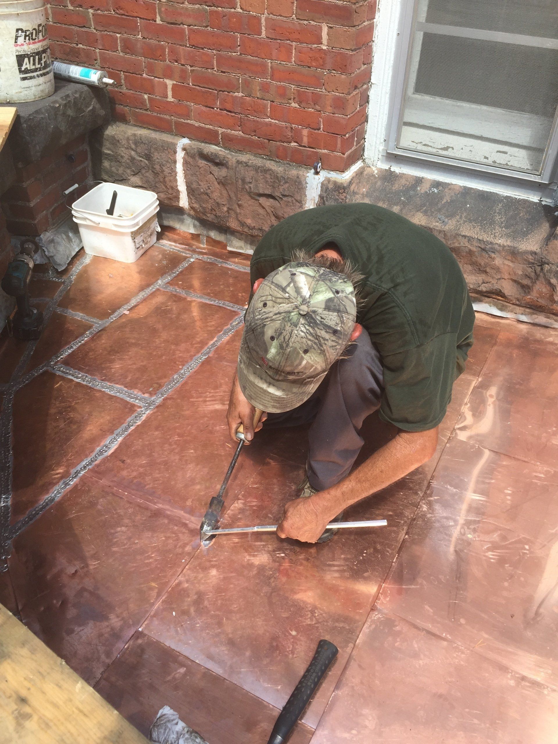 A man is kneeling down on a tiled floor with a hammer.