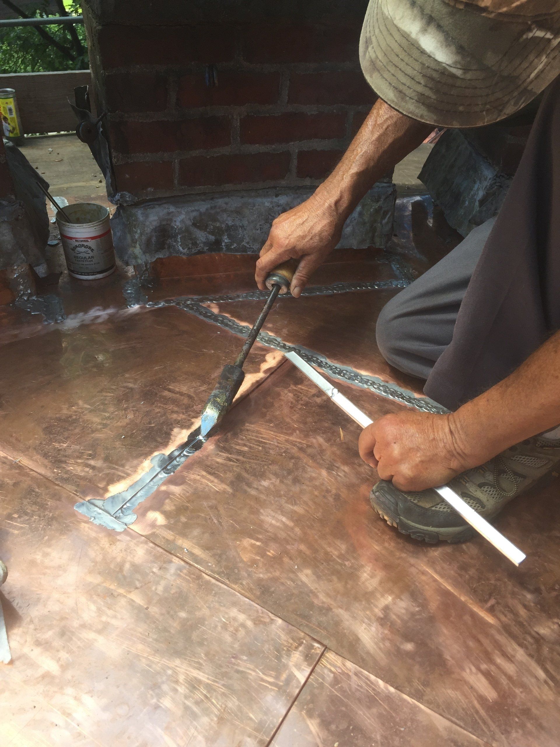 A man is working on a copper roof with a hammer.