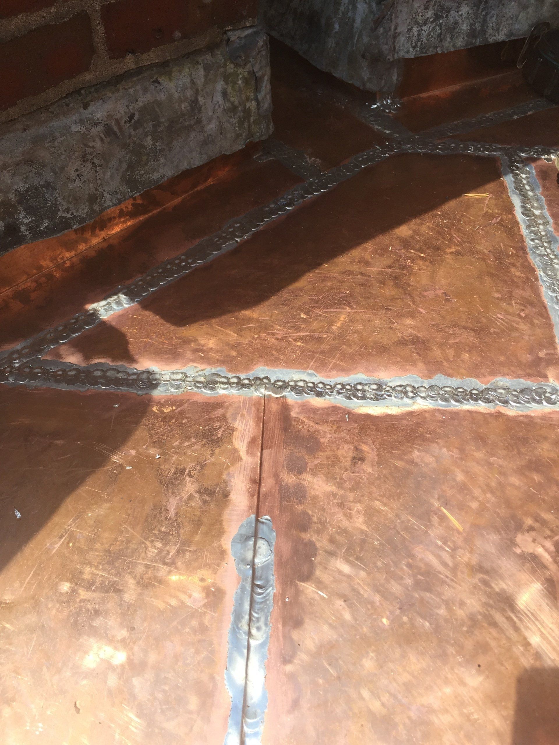 A close up of a copper floor with a brick wall in the background.