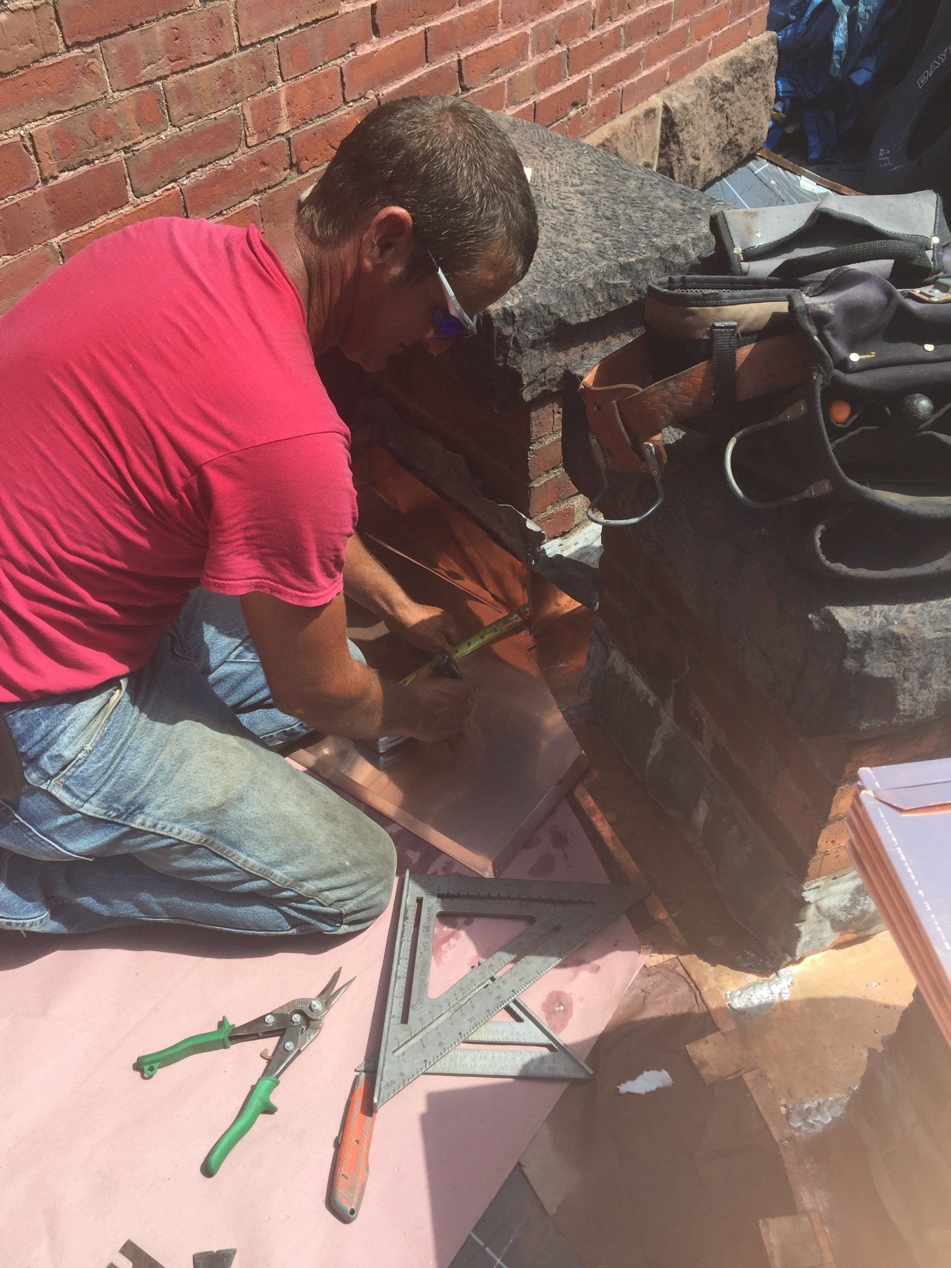 A man in a red shirt is kneeling down and working on a roof.