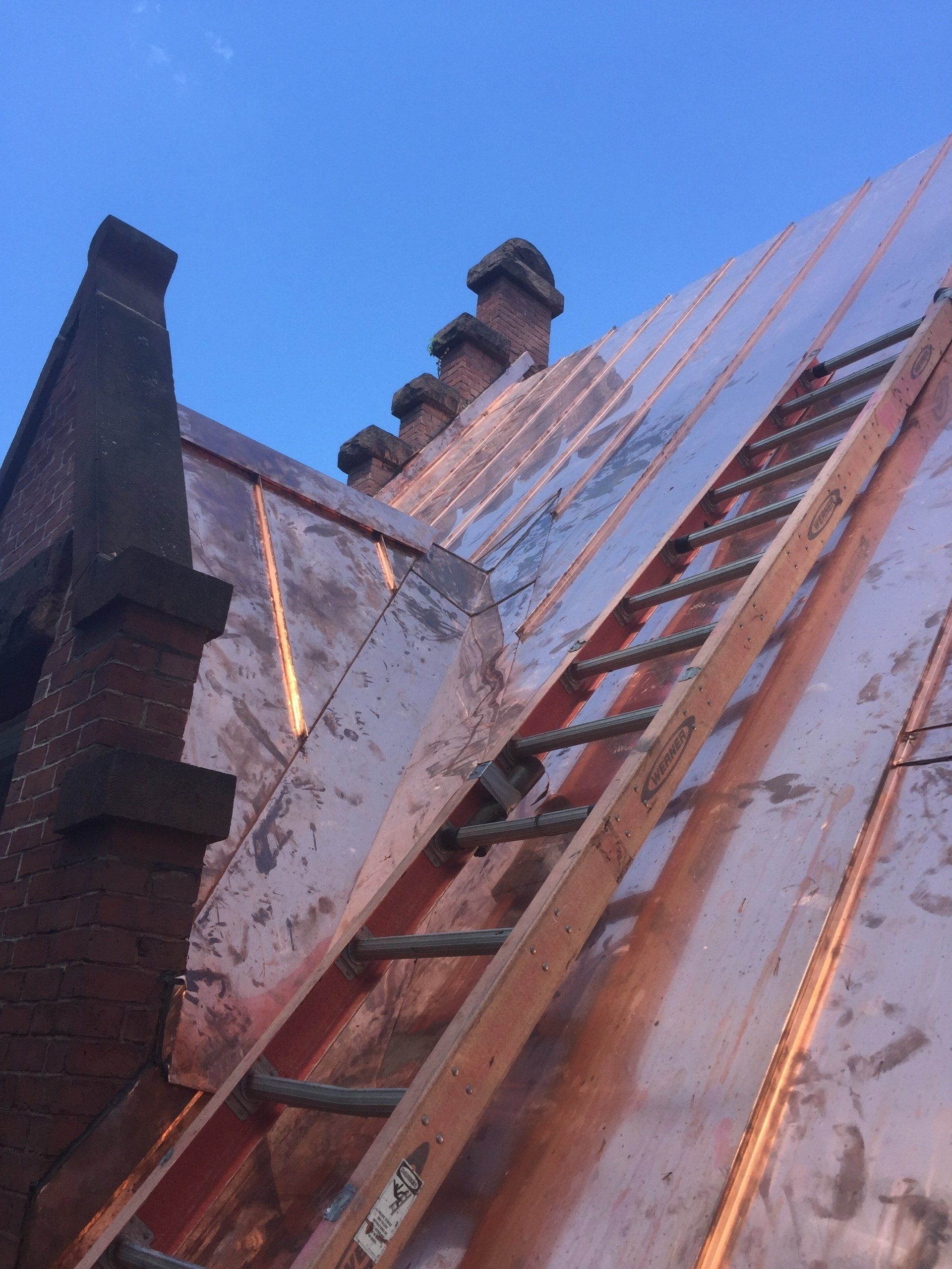 A ladder is sitting on top of a copper roof.