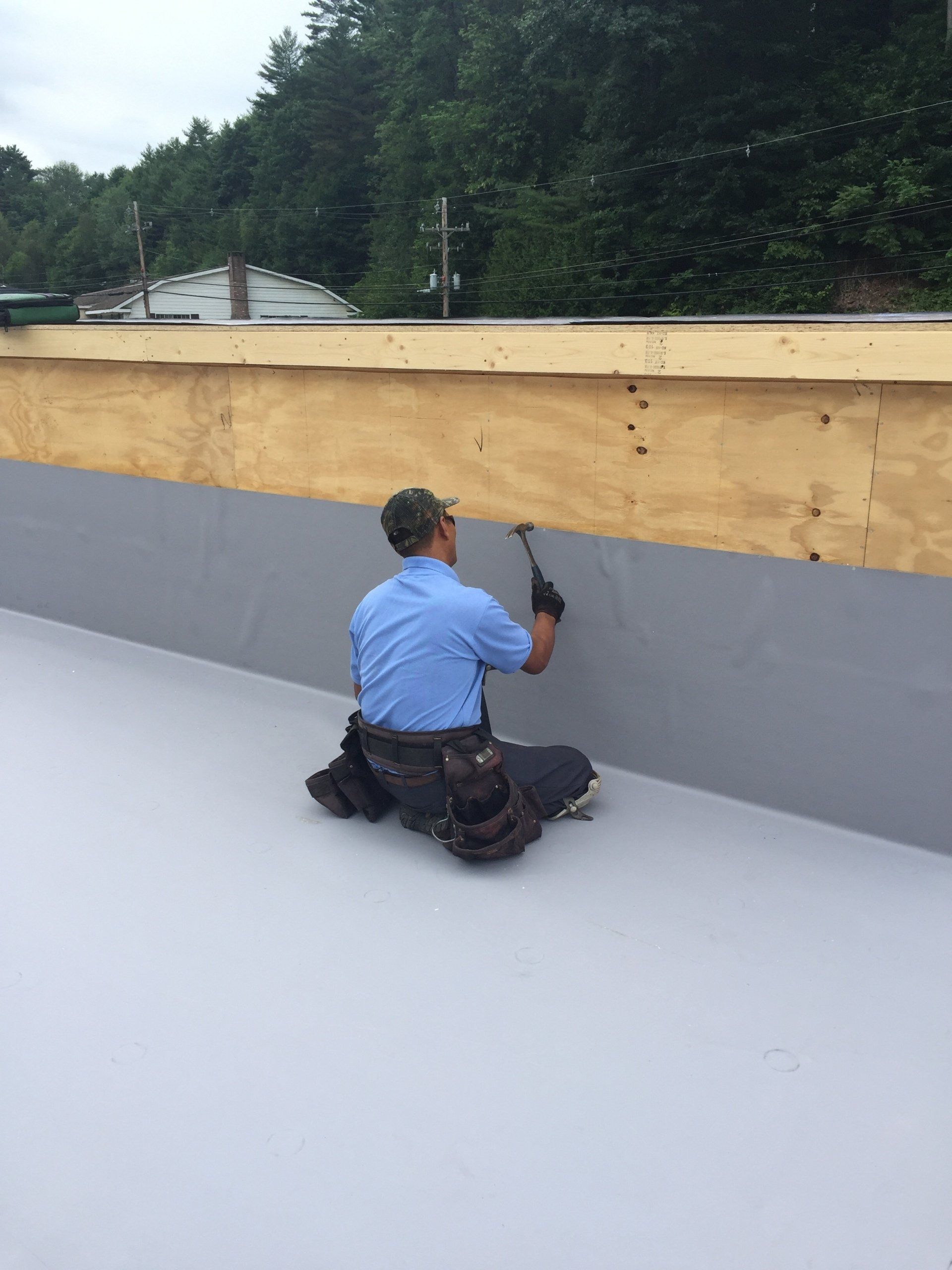 A man is kneeling on the ground working on a roof.