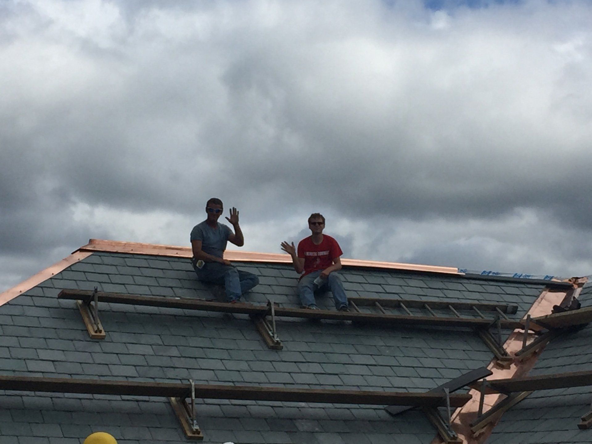 Two men are sitting on top of a roof with a ladder.